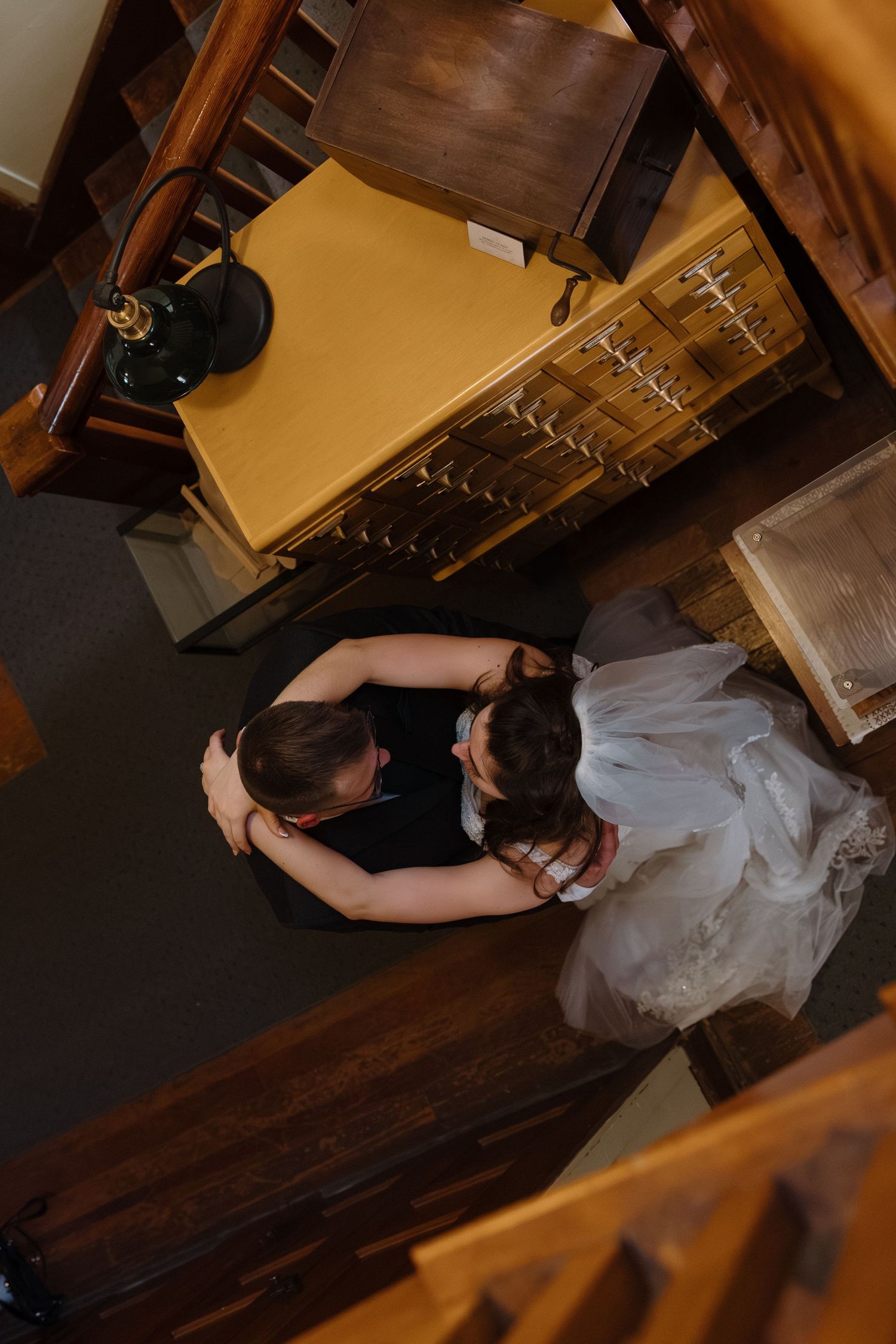 Aerial view of bride and groom sharing a tender dance embrace on a wooden floor surrounded by vintage furniture.