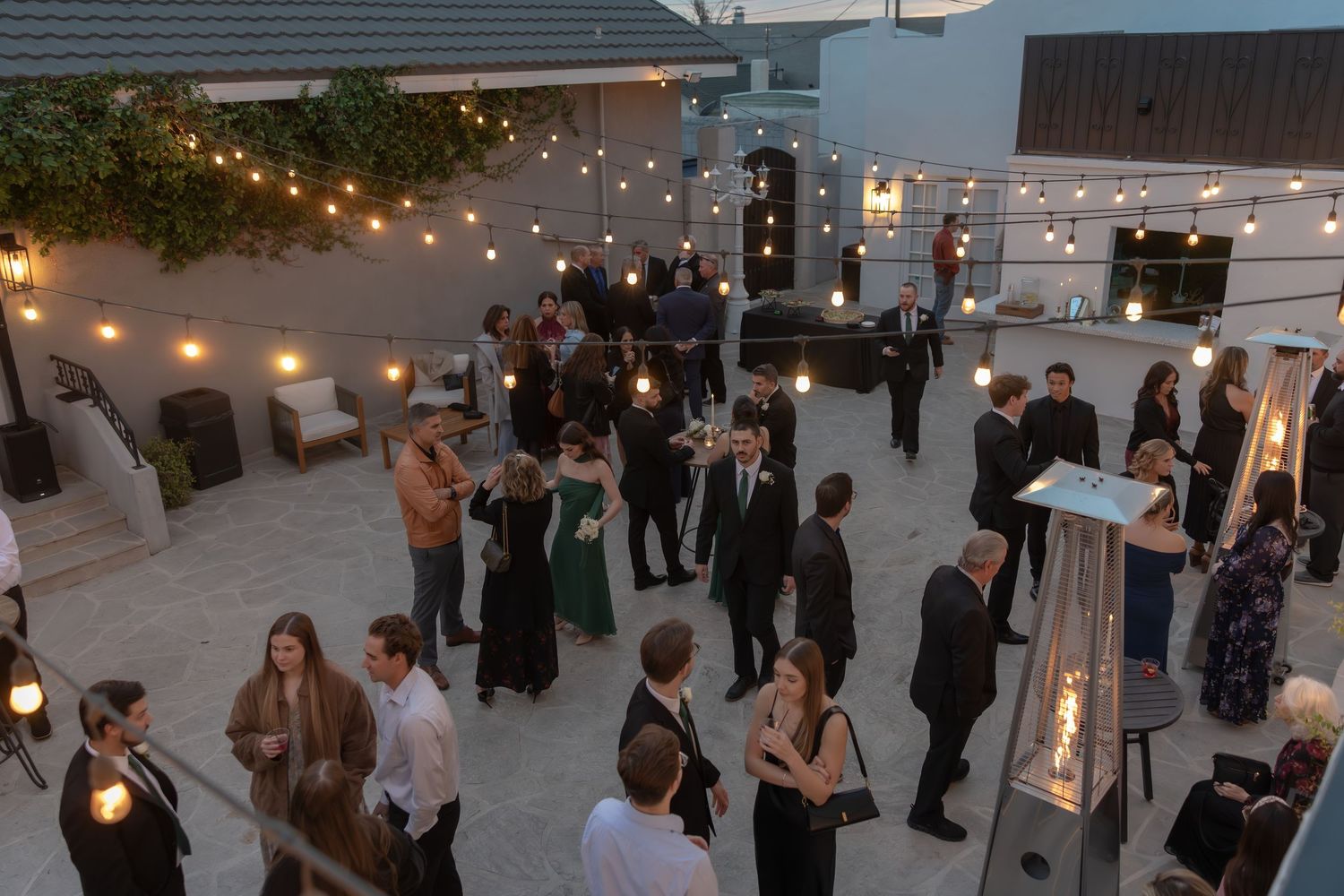 Aerial view of elegantly dressed wedding guests socializing at an outdoor evening reception.