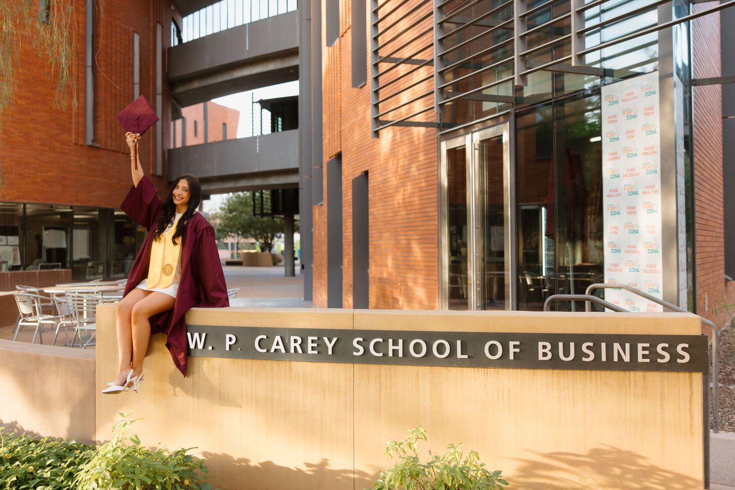 Graduate poses outside the W. P. Carey School of Business building, holding a maroon tassel at Arizona State University.