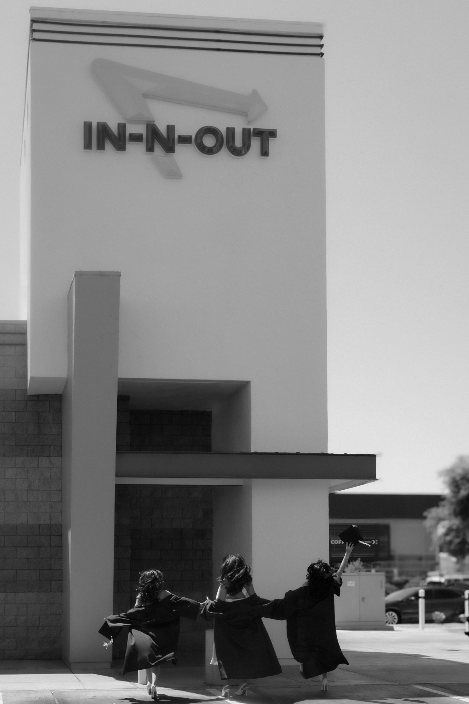 Black and white photo of three graduates tossing caps outside In-N-Out Burger.