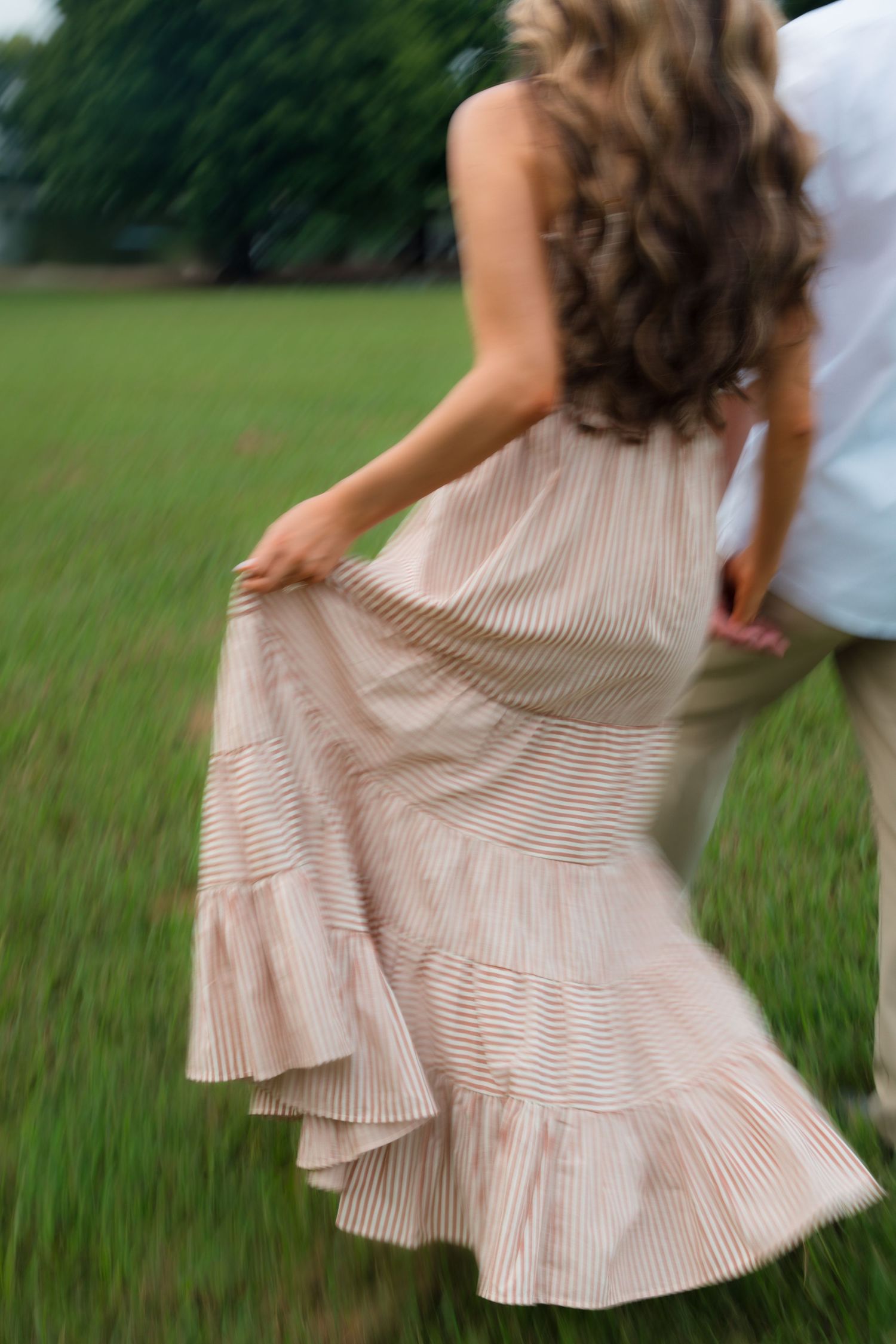A woman in a flowing striped dress dances with a man in a green field, her hair and skirt swirling in motion.