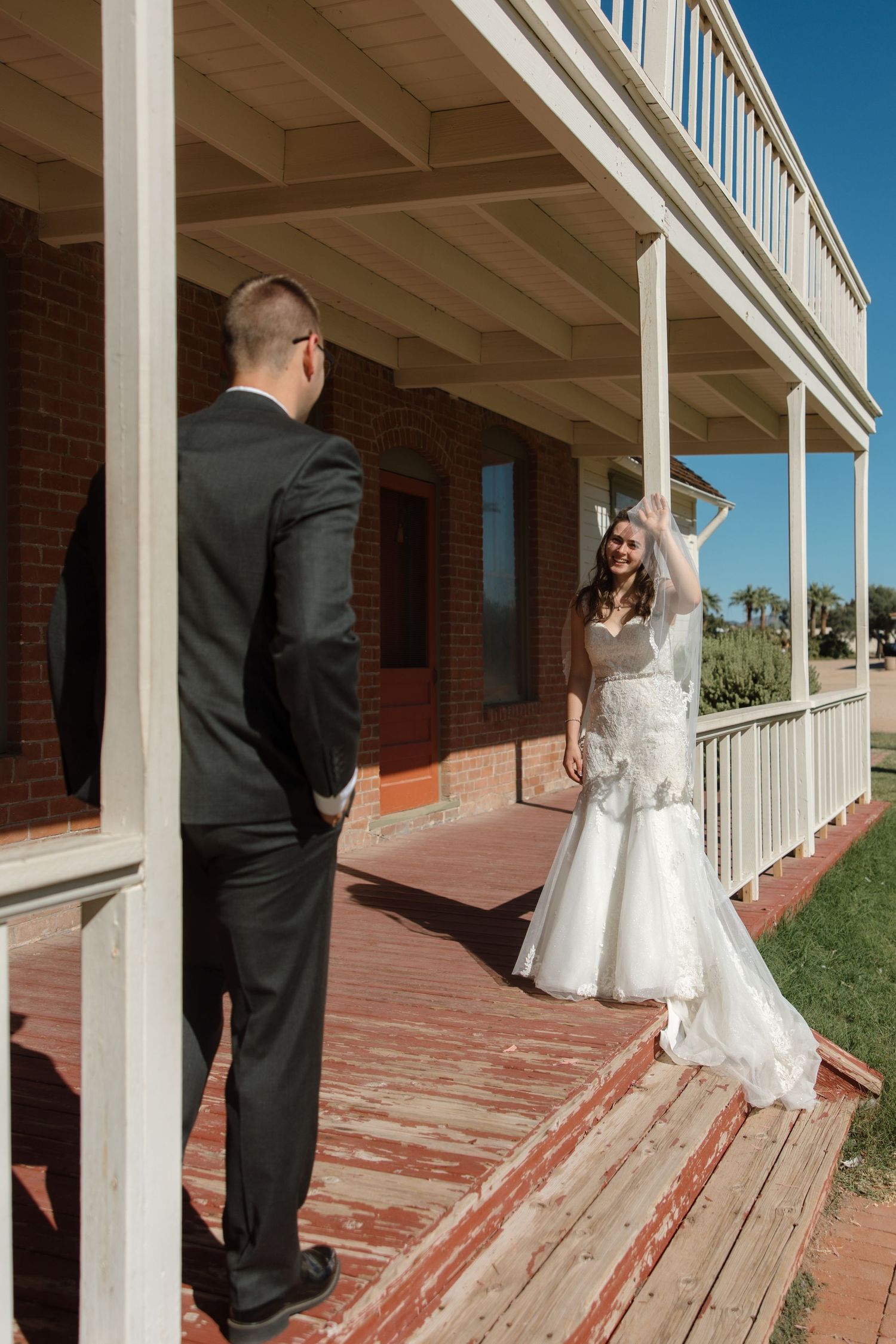 Bride smiles joyfully at groom during first look moment on rustic wooden porch.