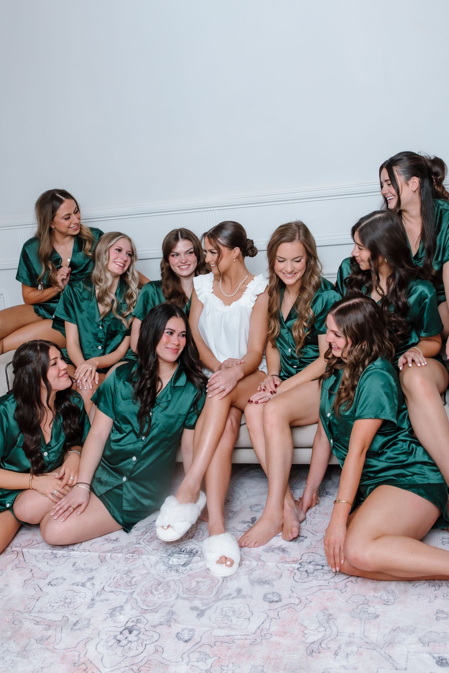 Bride surrounded by bridesmaids in emerald green satin pajamas laughing together before wedding.