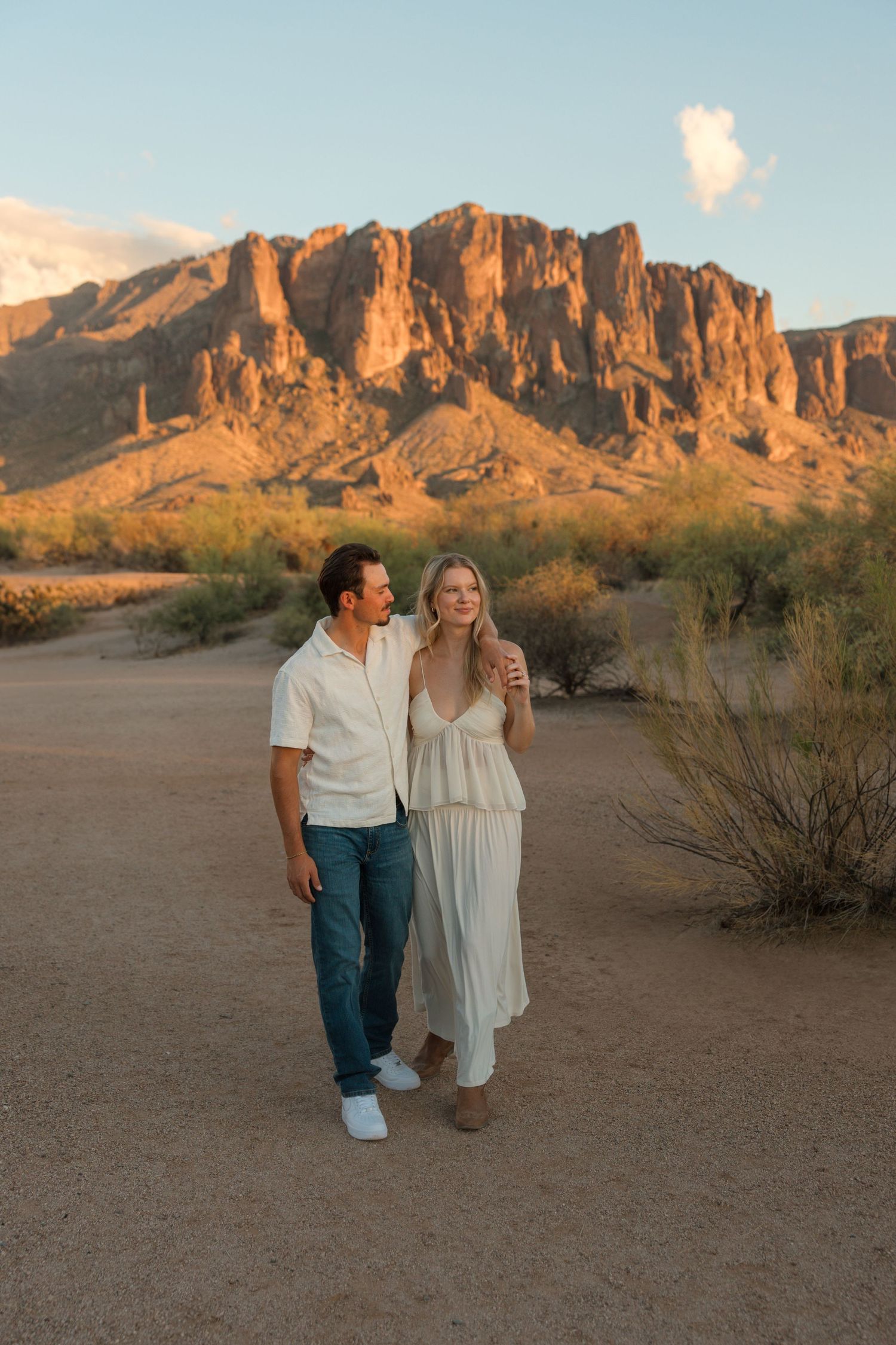 Couple walking in desert landscape with Superstition Mountains at golden hour in Arizona.