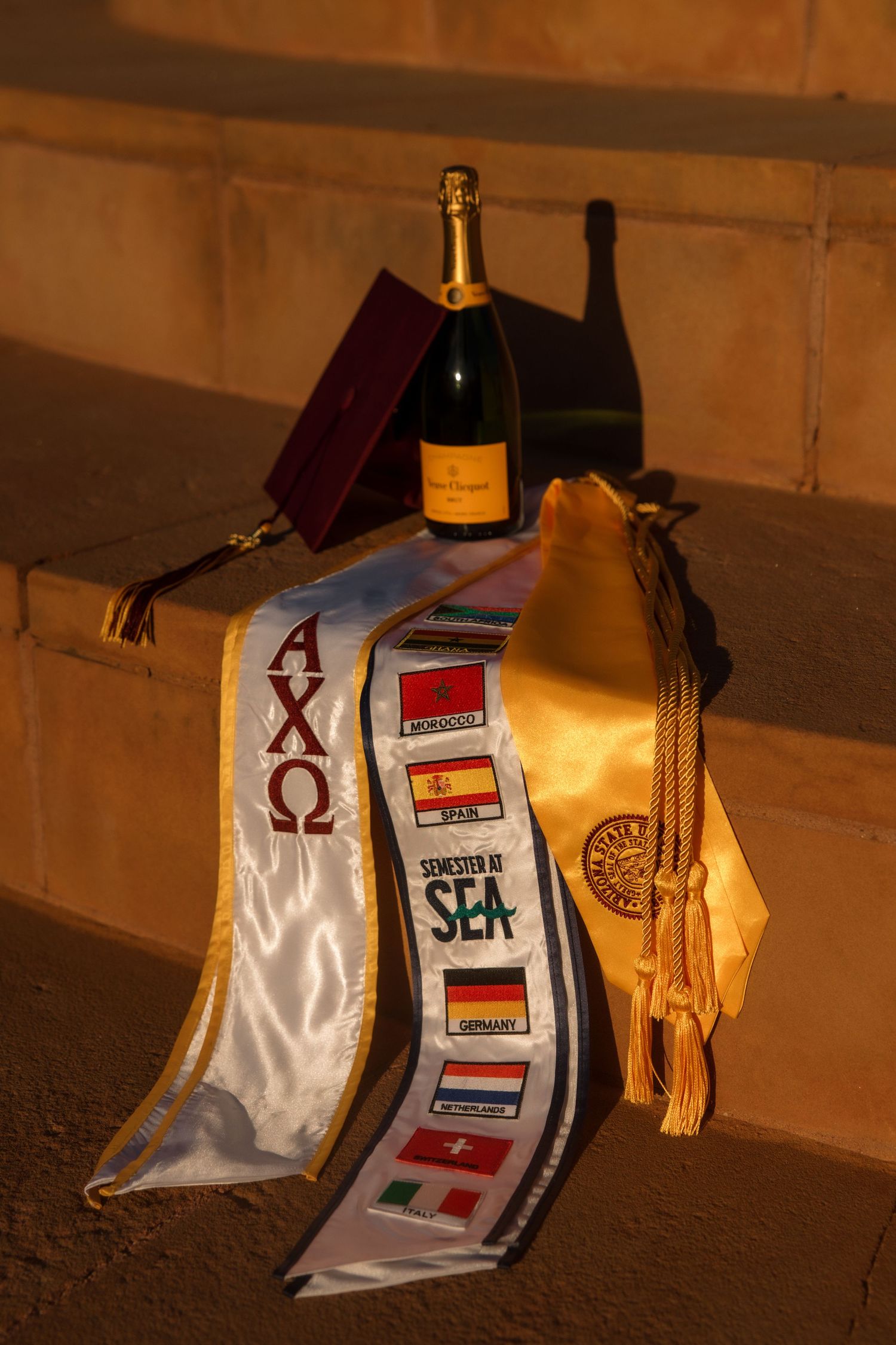 Graduation accessories including Chi Omega sash, Semester at Sea stole, gold tassel, cap and champagne bottle.
