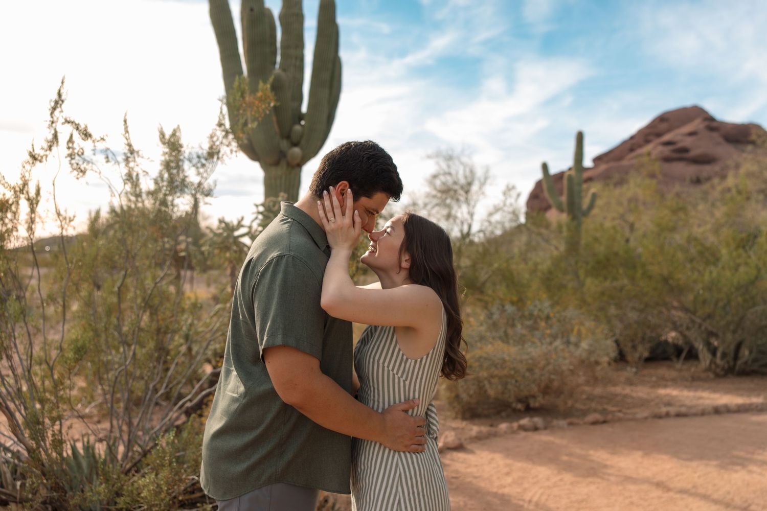 Couple sharing a romantic kiss in the Arizona desert with saguaro cactus and red mountains in the background.