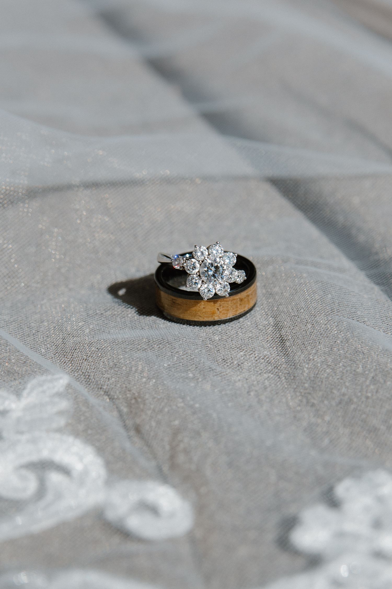 Elegant diamond flower cluster engagement ring resting on a wooden band atop a lace wedding veil.
