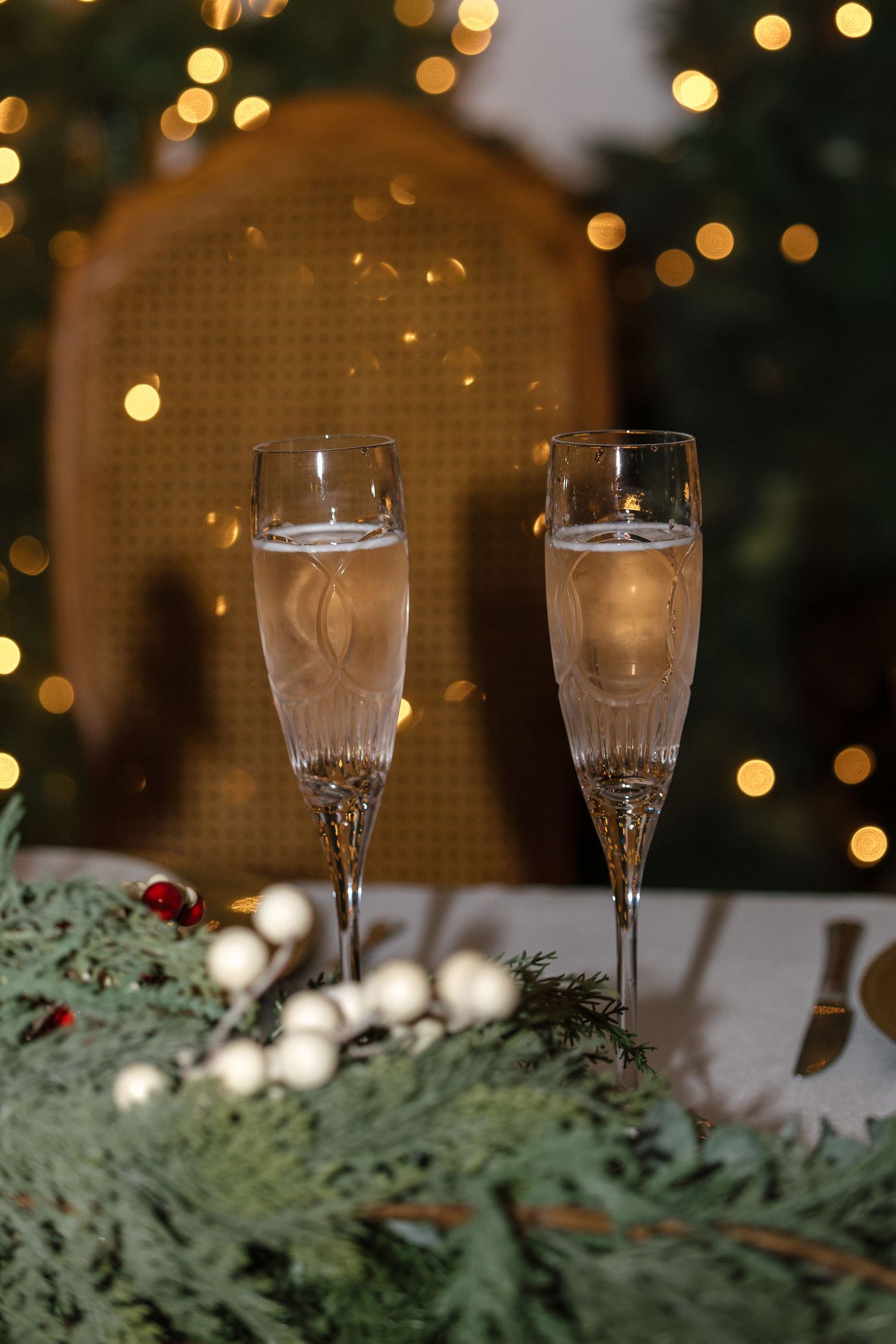 Two crystal champagne flutes filled with sparkling wine against a glowing Christmas tree backdrop.