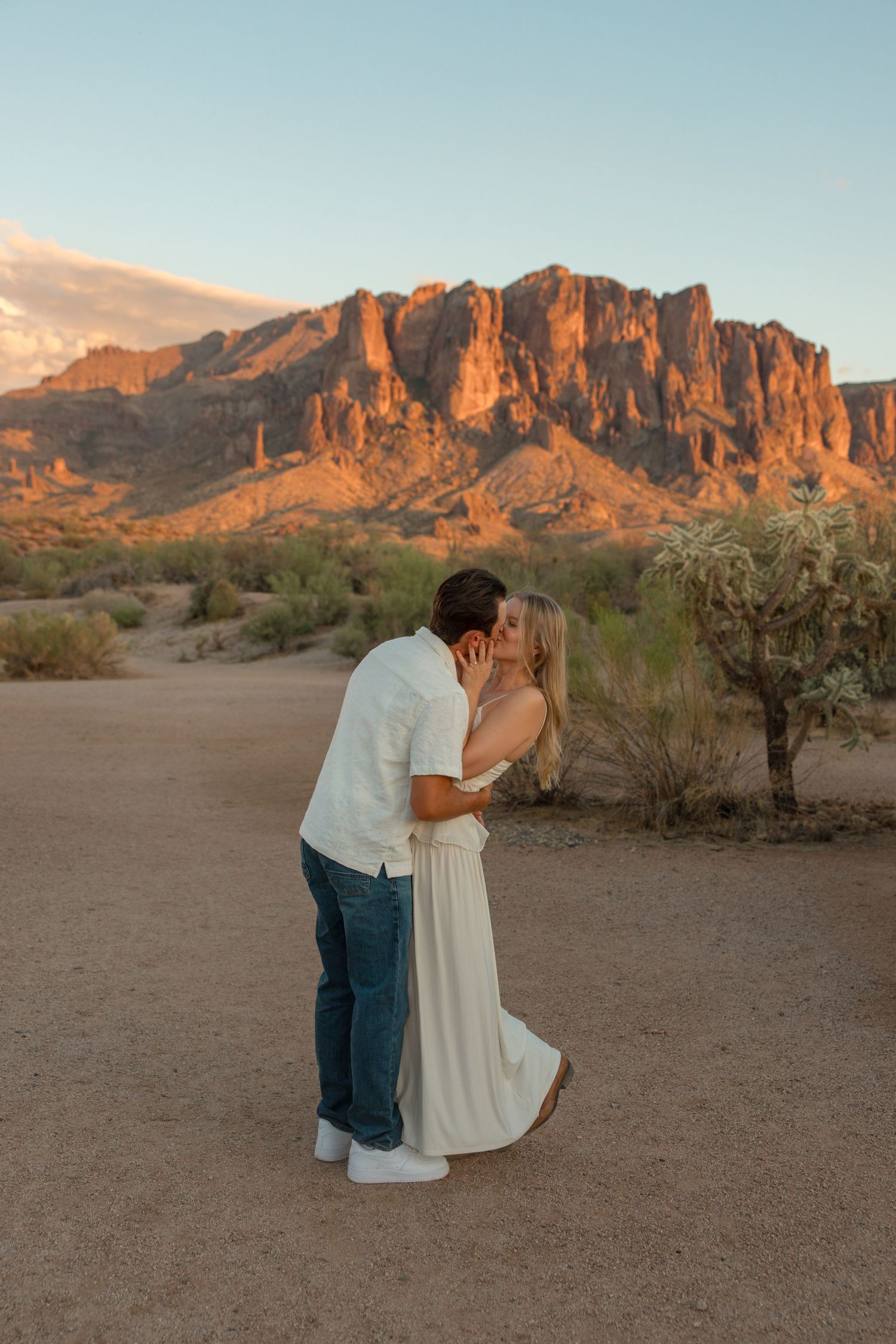 Couple sharing a romantic kiss at sunset with the Superstition Mountains glowing in the Arizona desert background.