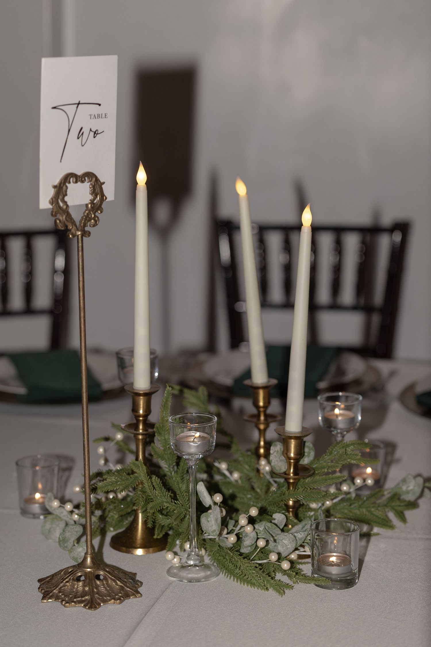 Elegant winter wedding table centerpiece with gold candlesticks, white taper candles, and greenery with white berries.