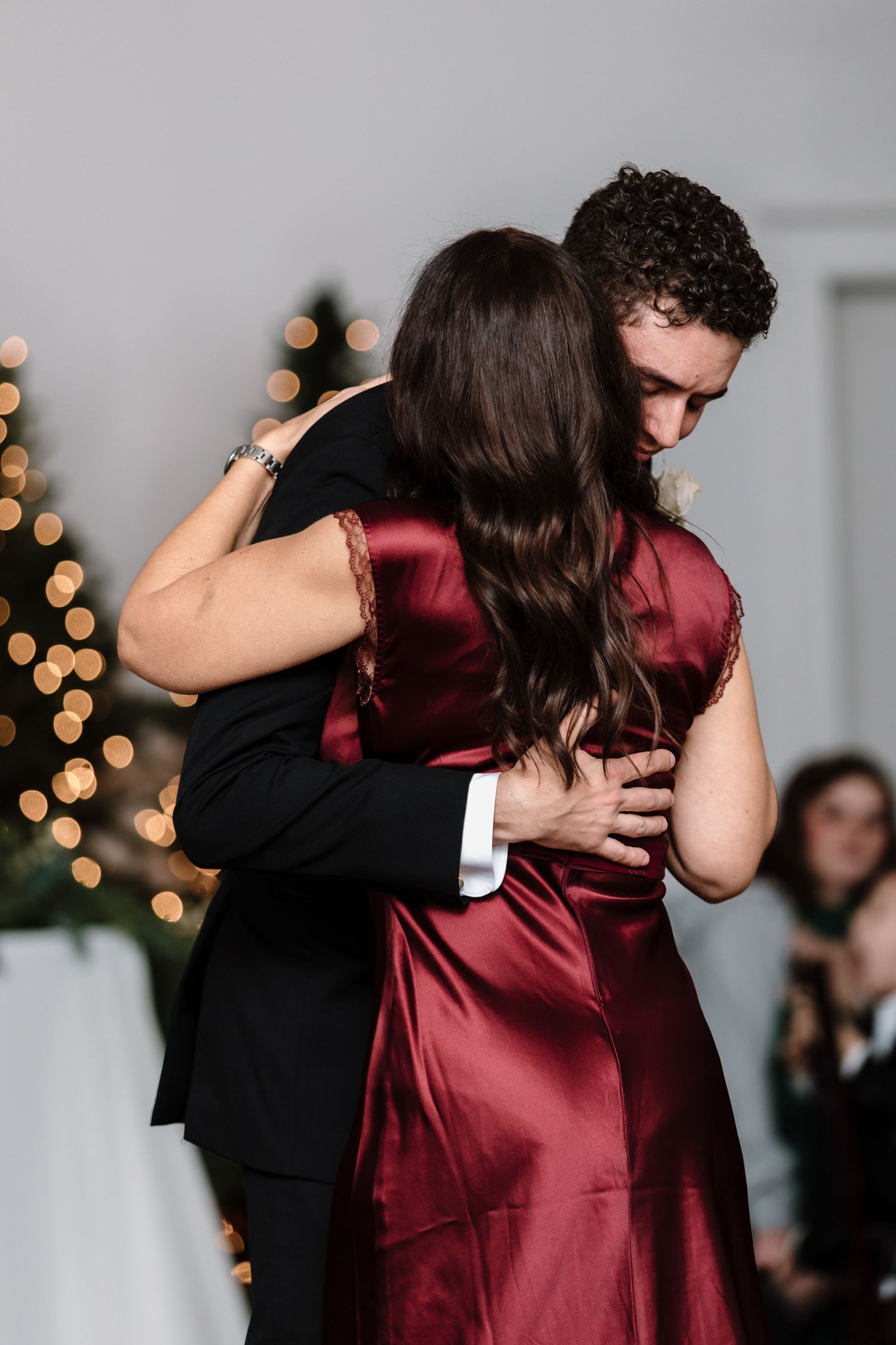 Groom shares emotional mother-son dance at wedding reception, both embracing in burgundy and black attire.