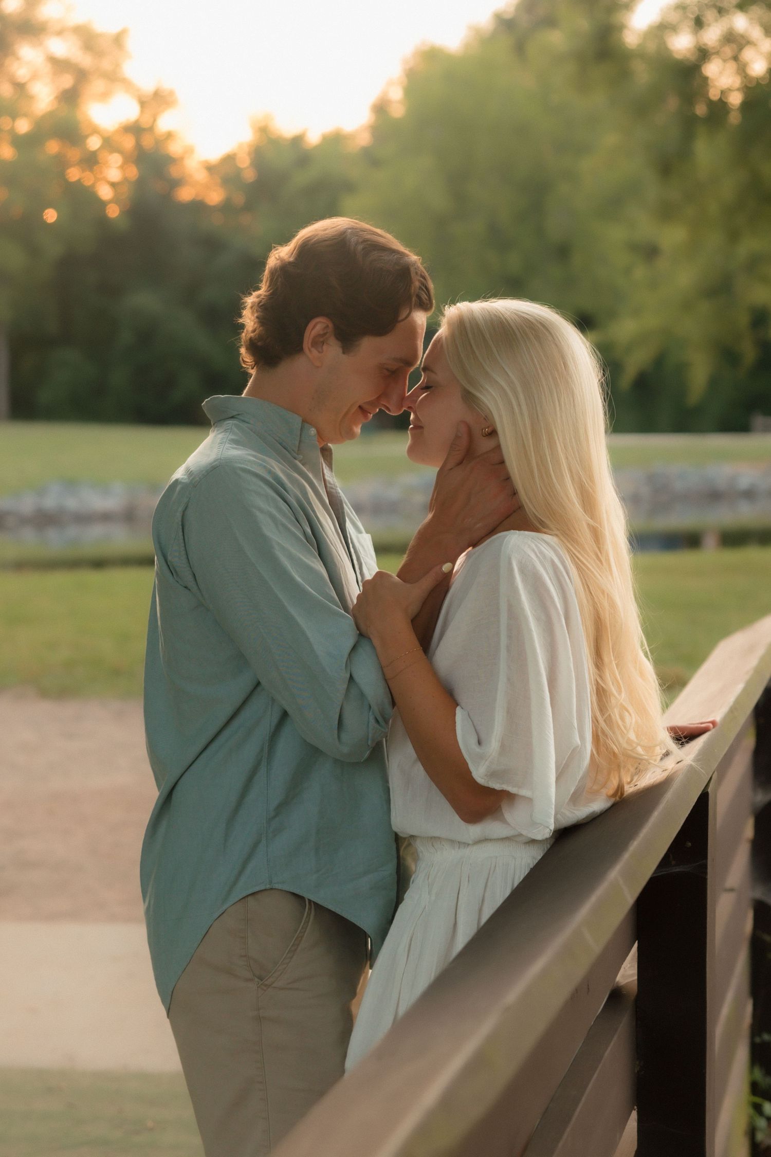 Couple sharing a romantic moment on a bridge at golden hour in a lush green park.
