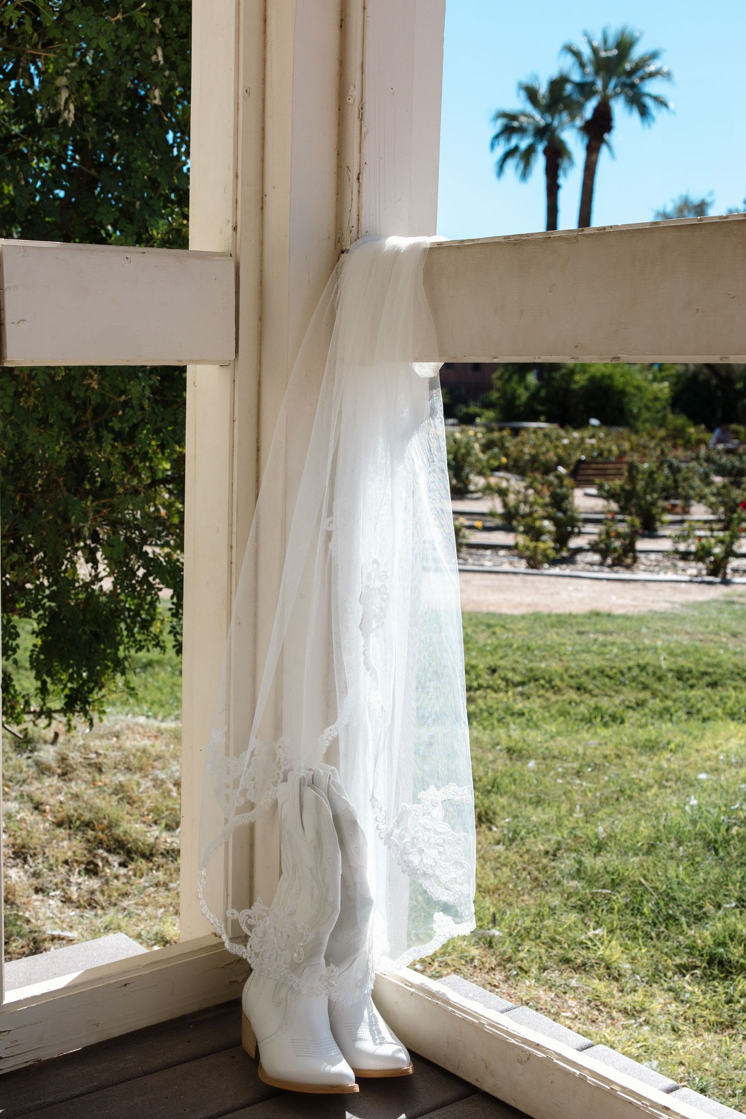 Bridal veil and white cowboy boots displayed on a sunlit porch with lush green garden in the background.