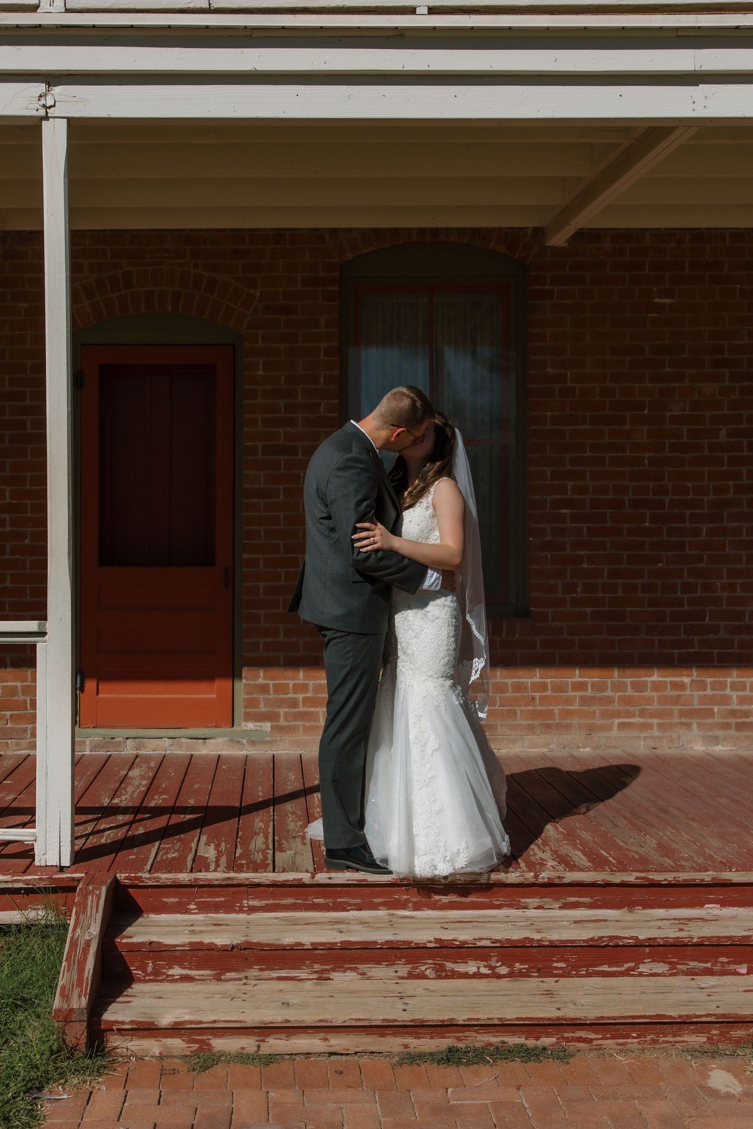 Bride and groom share an intimate embrace on weathered red steps of brick building.