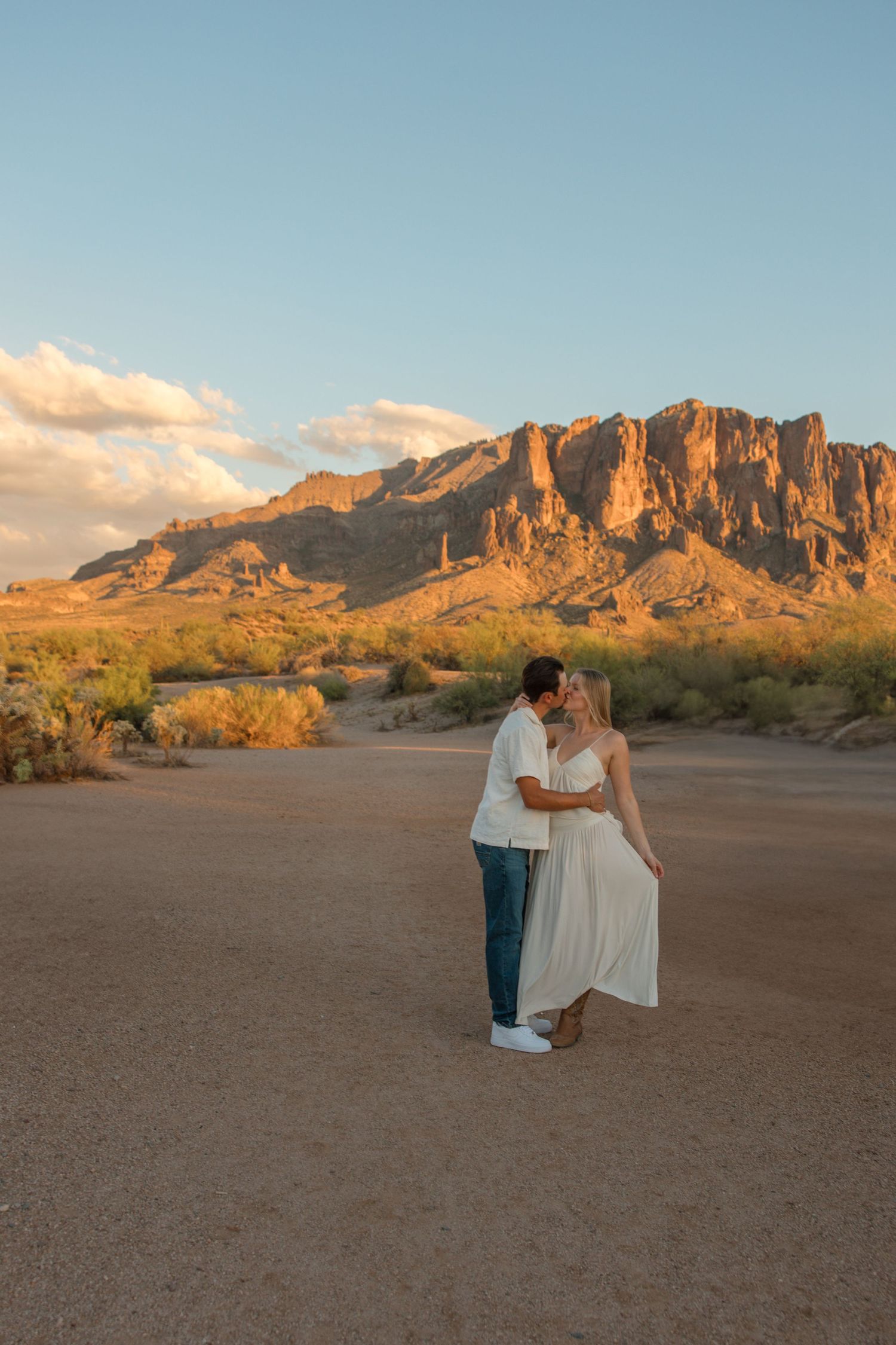 Couple sharing a romantic kiss at golden hour with the Superstition Mountains in the Arizona desert background.