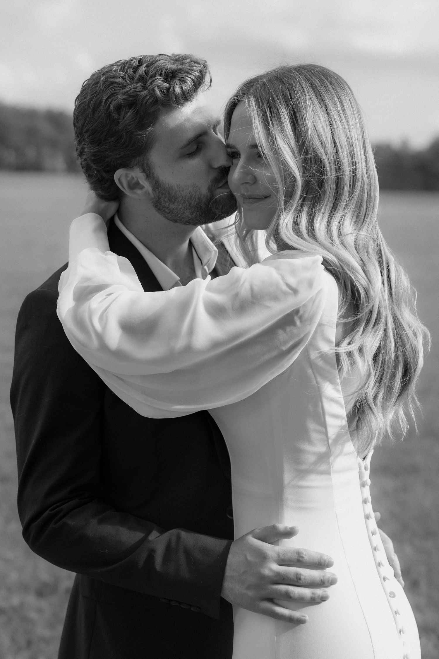 Black and white photo of a bride and groom sharing a tender kiss outdoors on their wedding day.