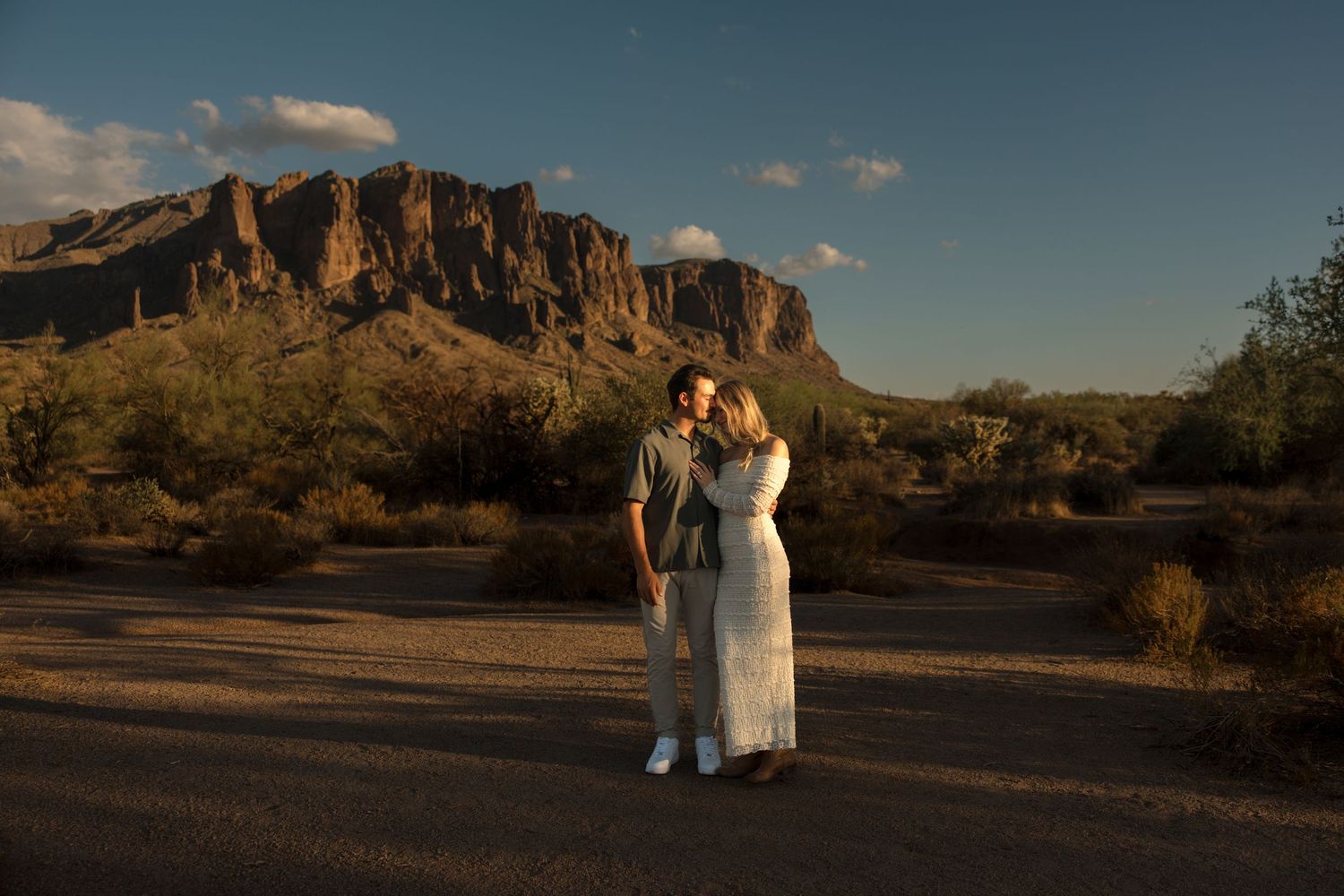 Couple embracing at golden hour with Superstition Mountains in the Arizona desert background.