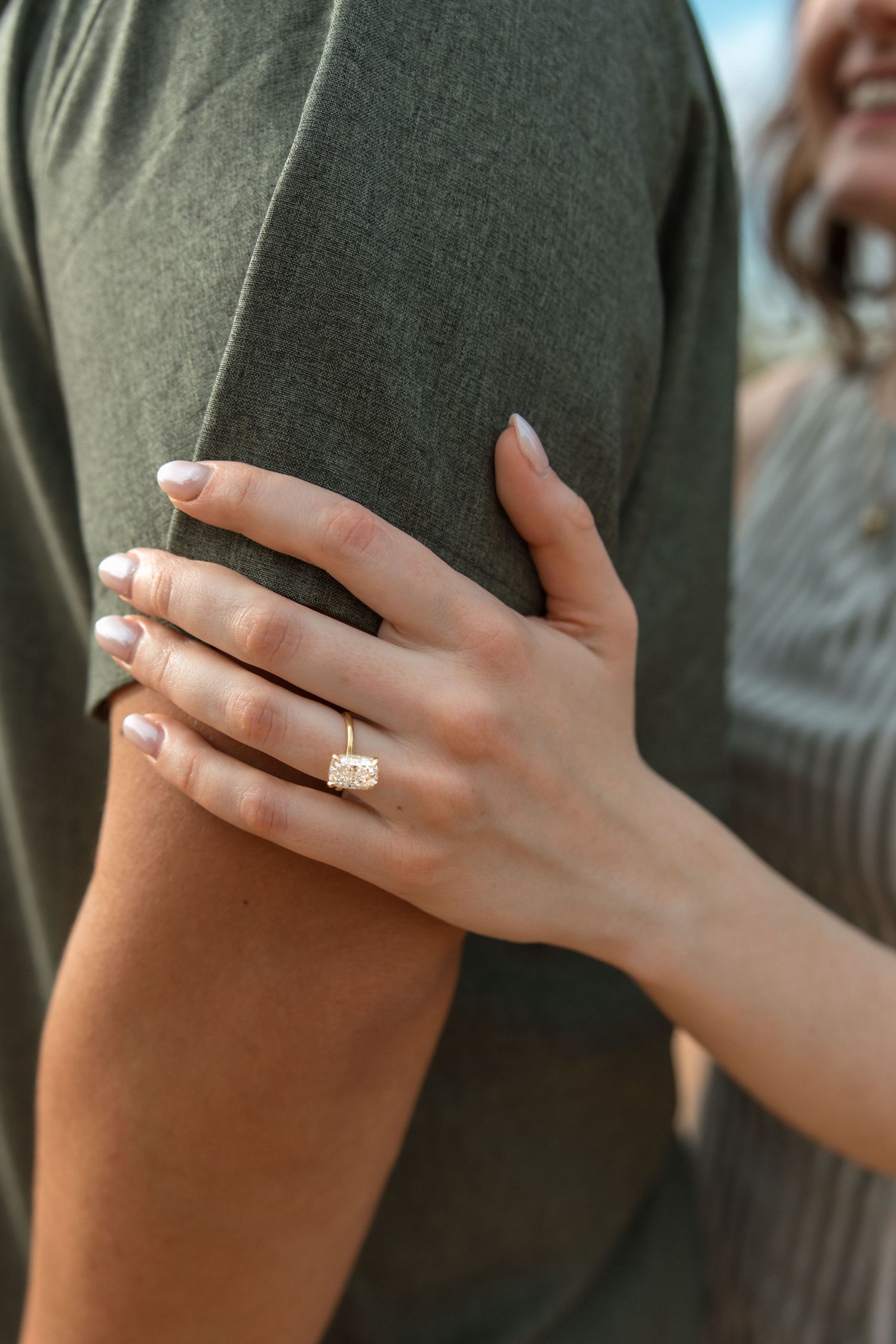 Close-up of a woman's hand wearing a gold diamond engagement ring while embracing her partner.