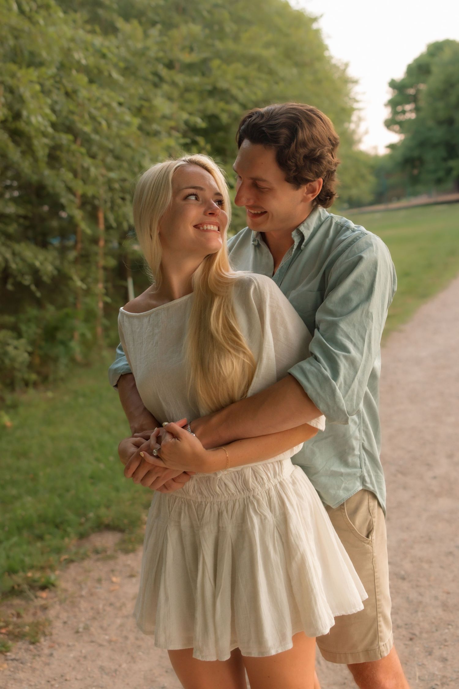 A couple shares a warm embrace on a gravel path in a green park at golden hour.