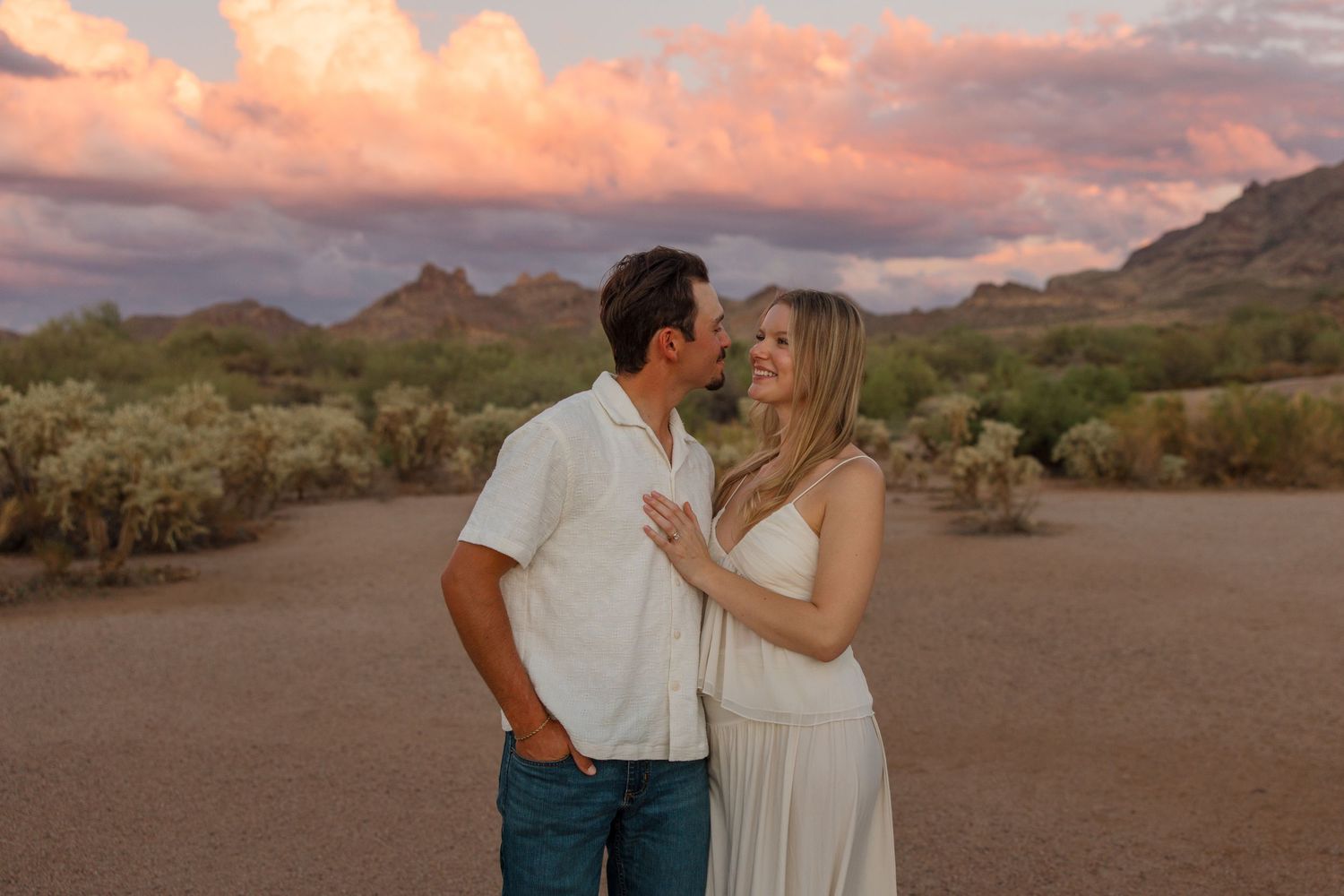 Couple sharing a romantic moment at sunset in the Arizona desert with pink clouds and mountain backdrop.