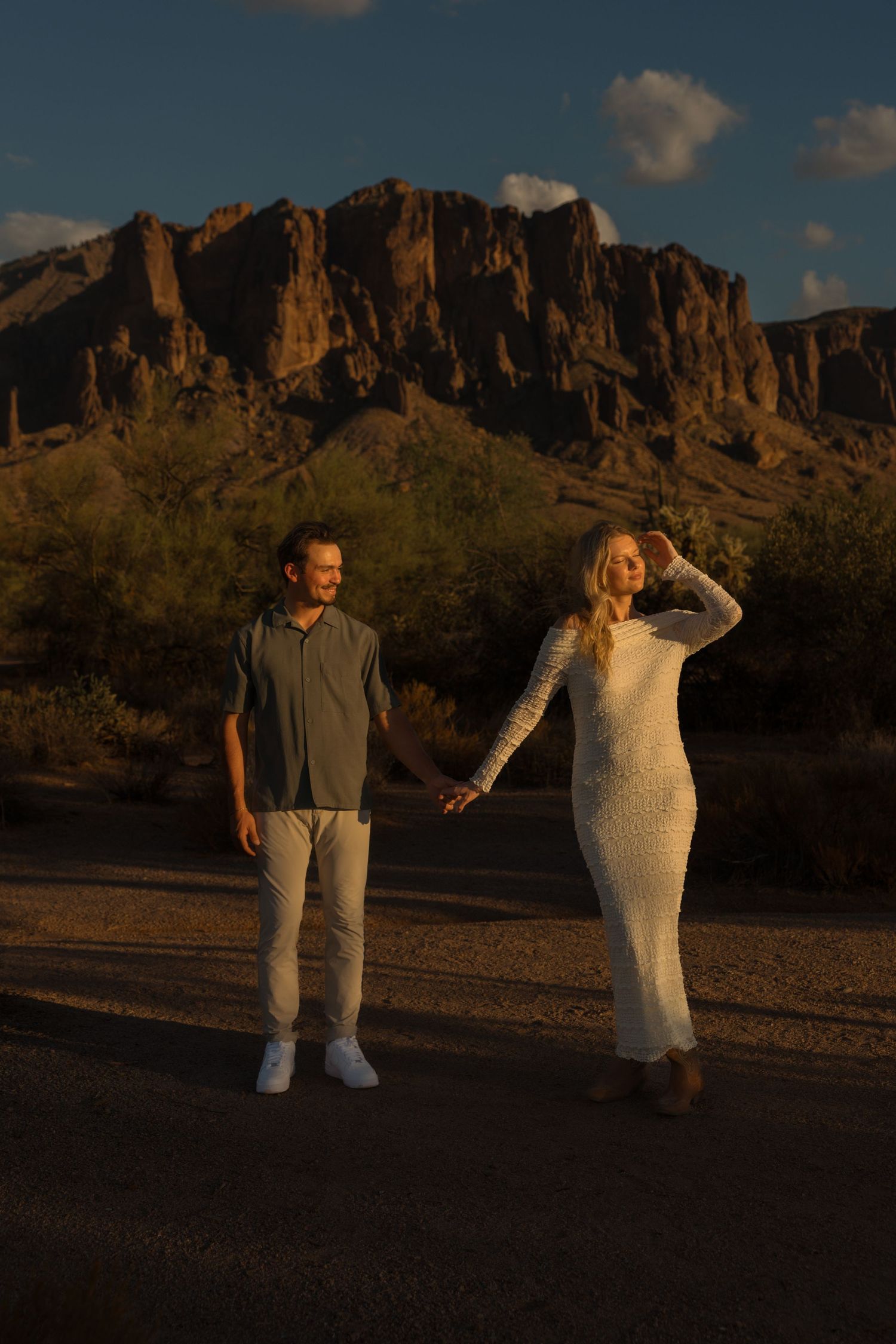 Couple holding hands at golden hour with Superstition Mountains backdrop in Arizona desert landscape.