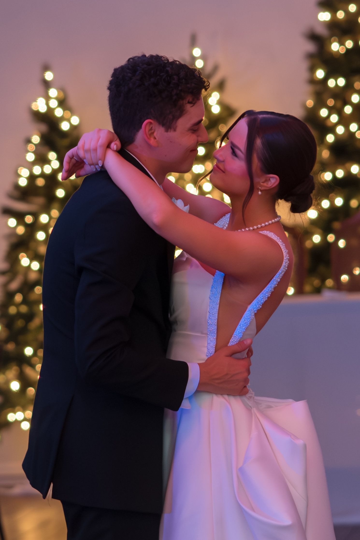Newlyweds share an intimate moment during first dance surrounded by sparkling Christmas tree lights at wedding reception.