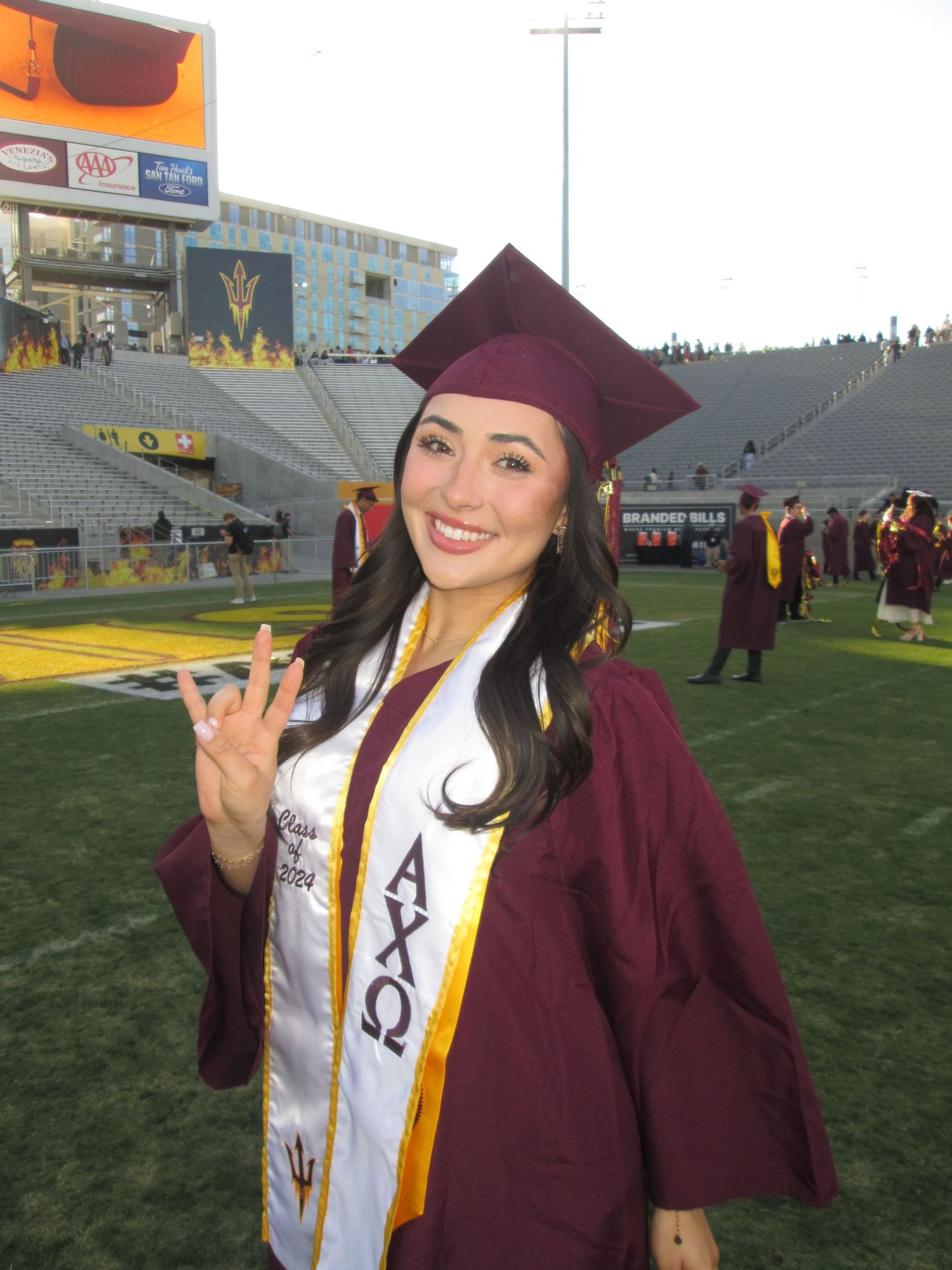 Female graduate in maroon cap and gown with Alpha Chi Omega sash at Arizona State University graduation ceremony.
