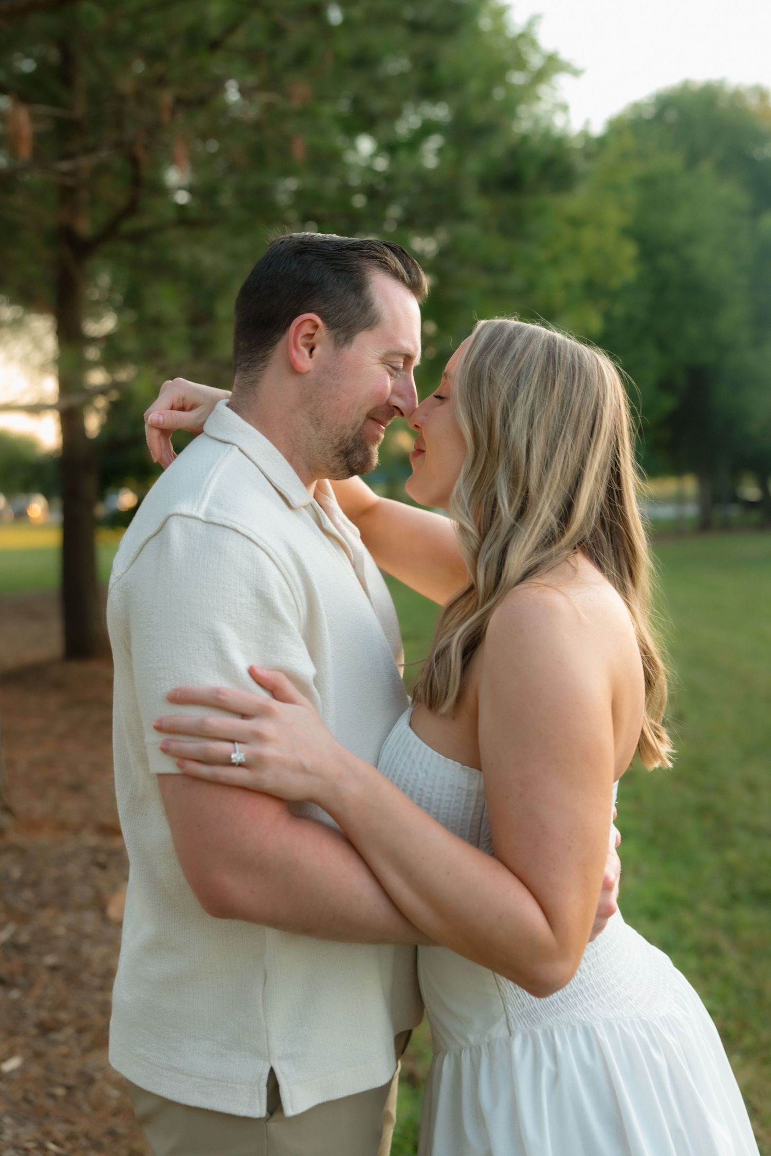 Couple embracing and leaning in for kiss in golden hour park setting during engagement photography session.