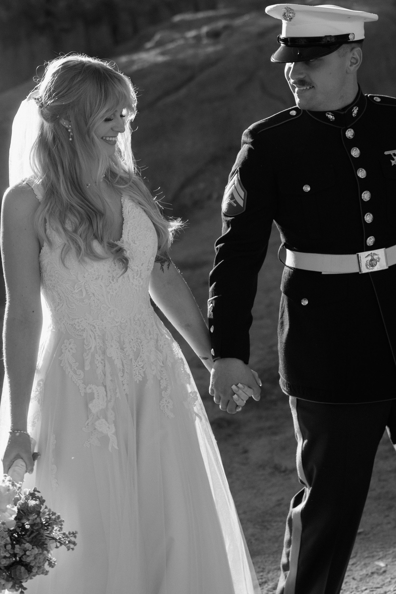 Black and white photo of smiling bride and Marine groom walking hand in hand.