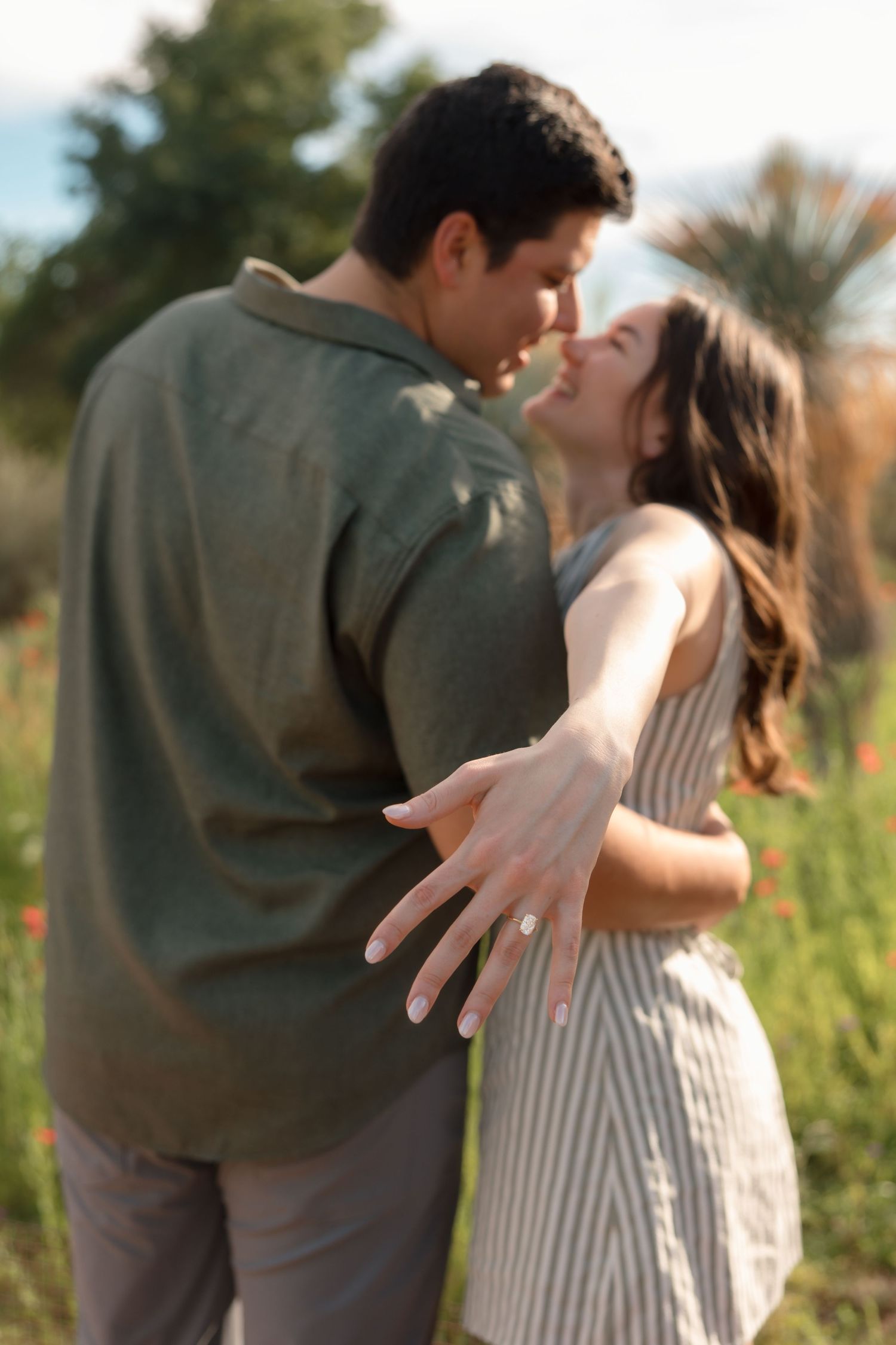 A couple shares a romantic moment in a flower field, with an engagement ring visible on the womans hand.