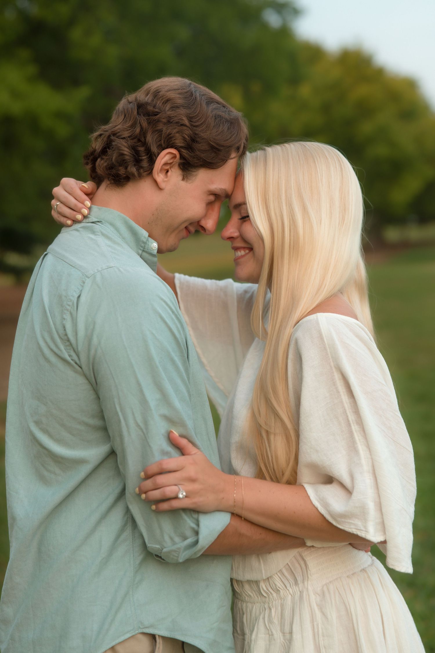 Happy couple touching foreheads and embracing in a lush green park at sunset.