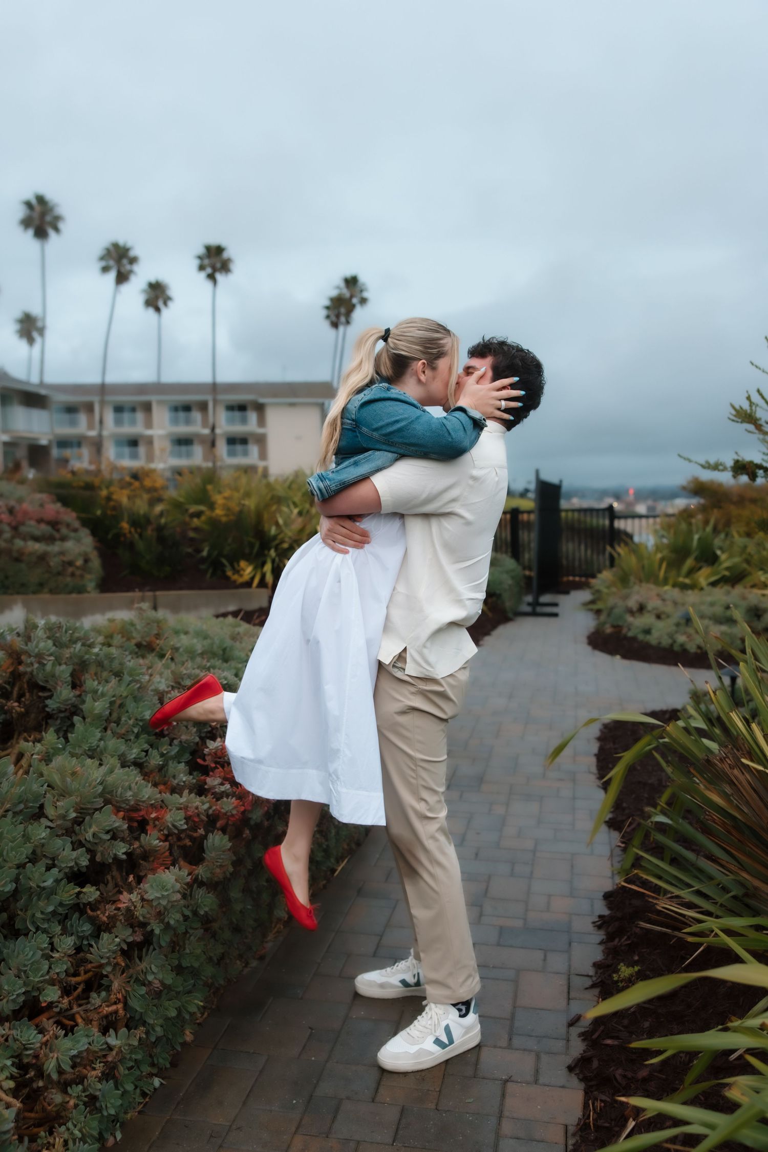 Man lifting woman in a kiss outdoors near palm trees after a marriage proposal.