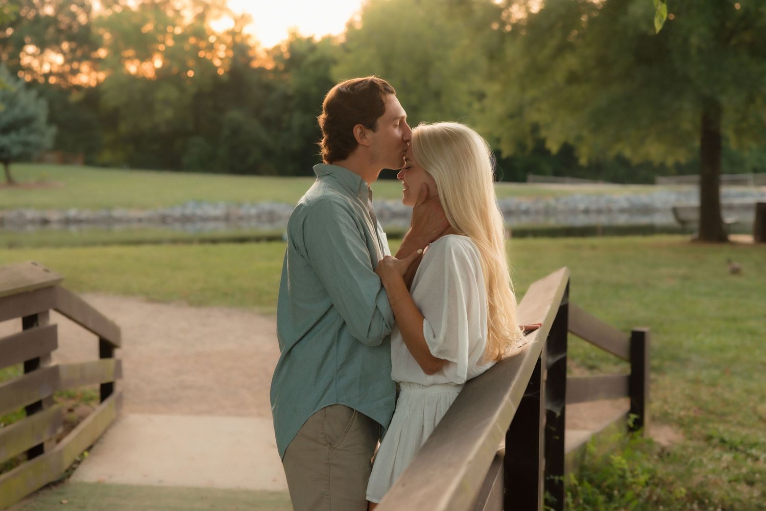 A couple leans in for a romantic kiss on a wooden bridge during a warm golden sunset.