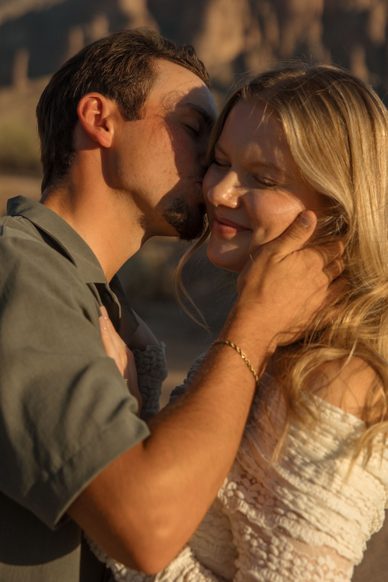 A couple shares a tender moment at golden hour, man gently cupping woman's face for a kiss outdoors.