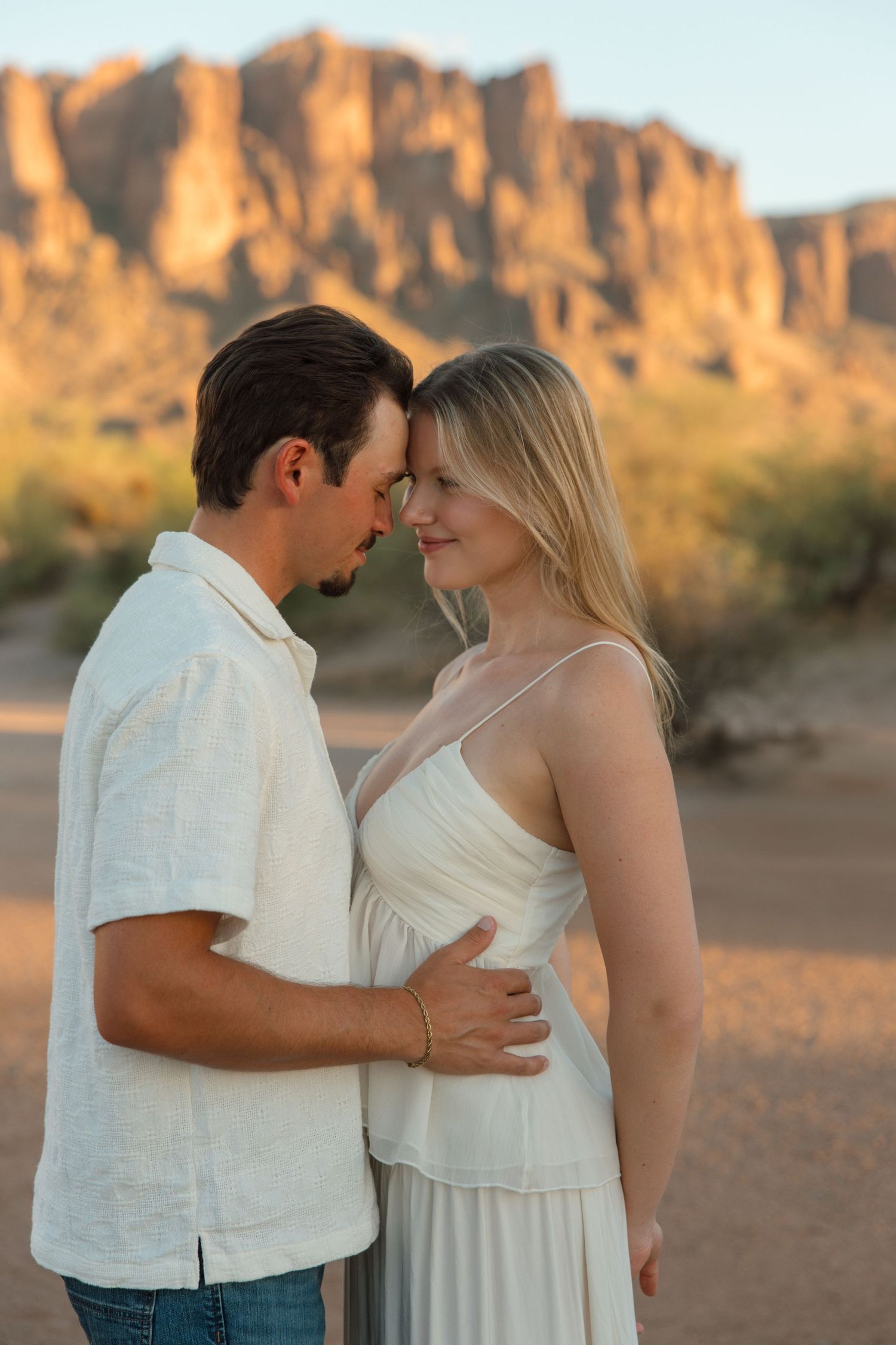 Couple sharing a romantic moment in the desert with Superstition Mountains at golden hour.