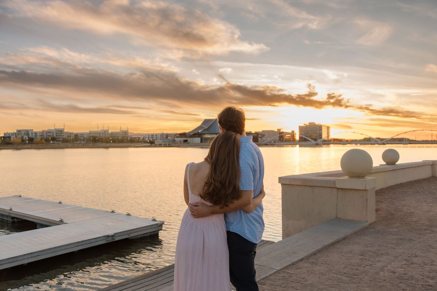 Couple standing together watching a stunning sunset over a calm lake with a city skyline view.
