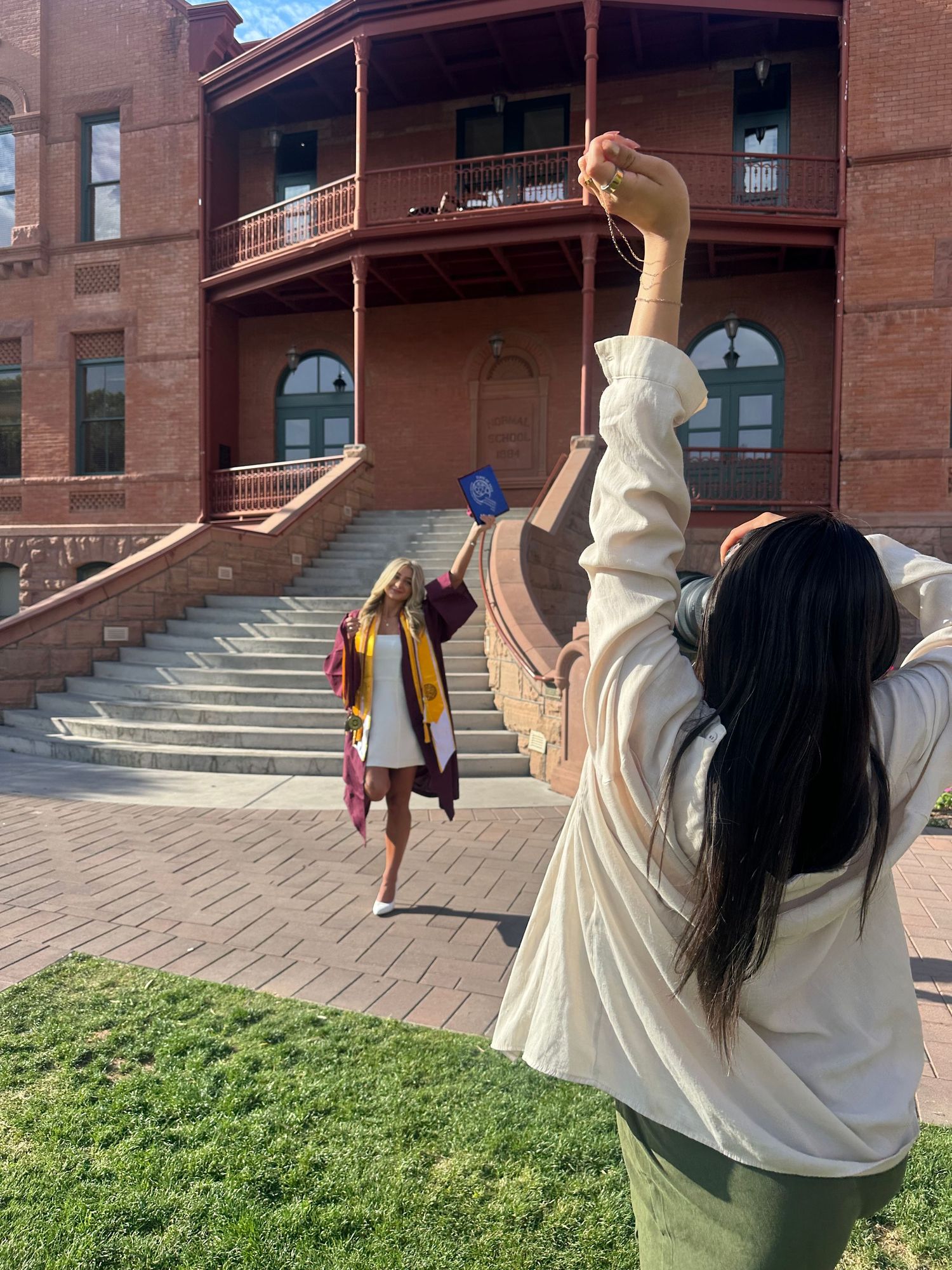 Photographer directs graduating student posing on steps of historic red brick university building.