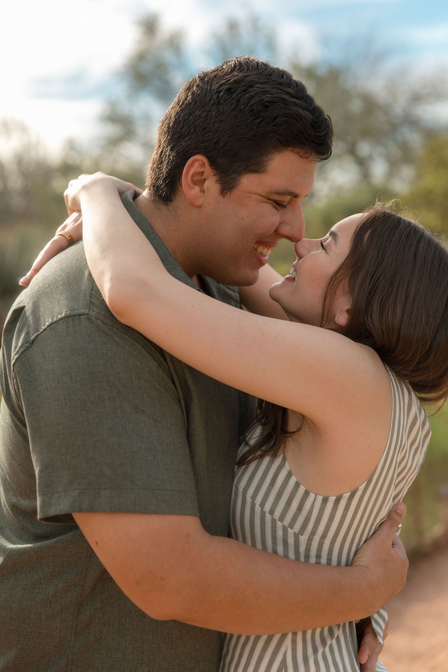 A romantic couple embracing and smiling at each other outdoors in a desert landscape at golden hour.