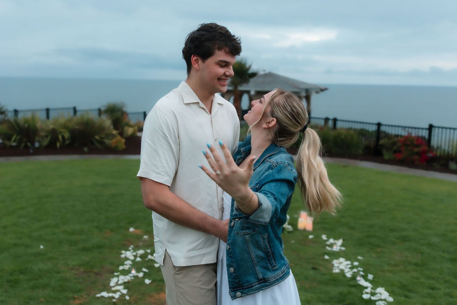 Happy newly engaged couple embracing outdoors showing off engagement ring by the ocean.