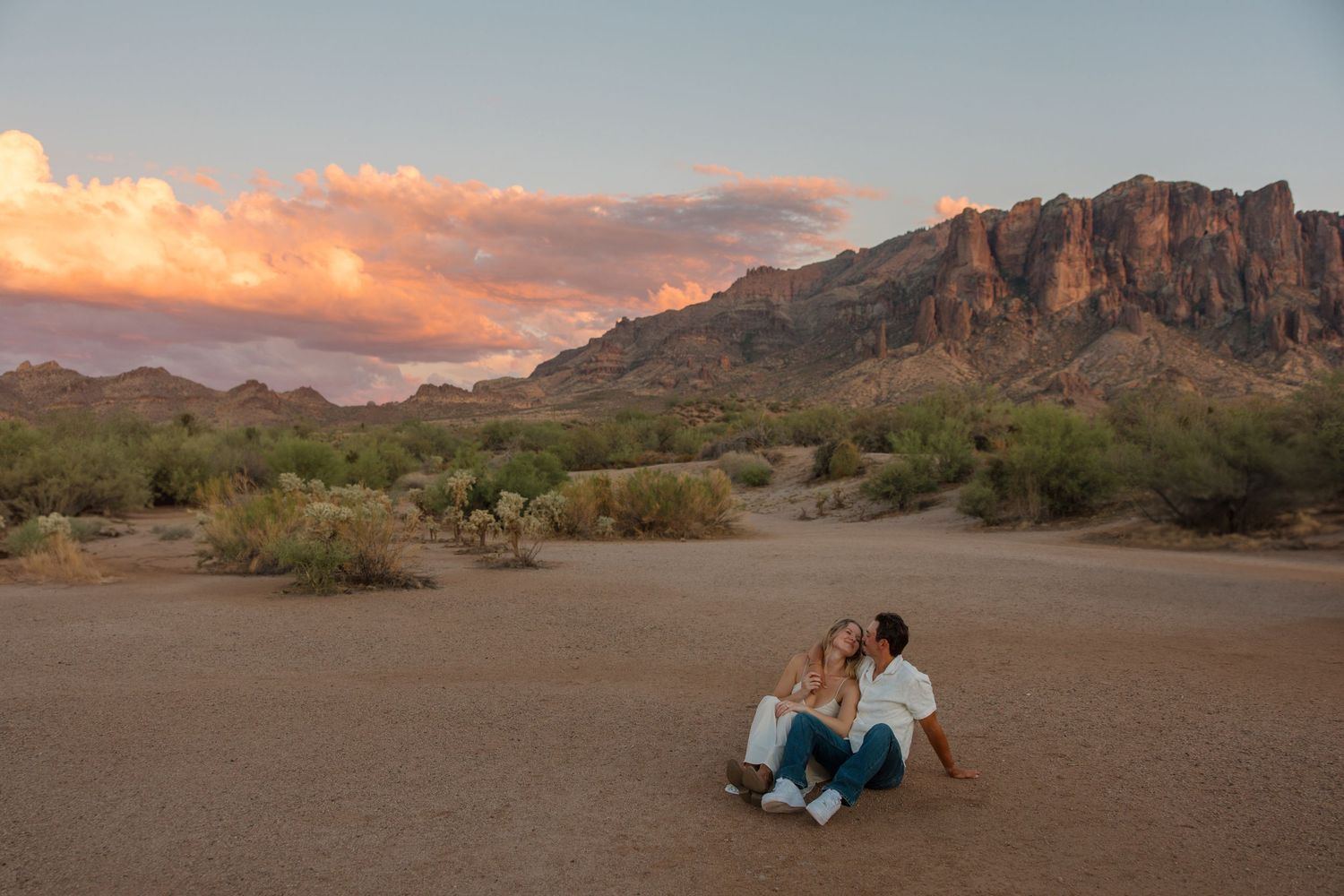 Couple sitting together on desert ground at sunset with Superstition Mountains in background, Arizona.