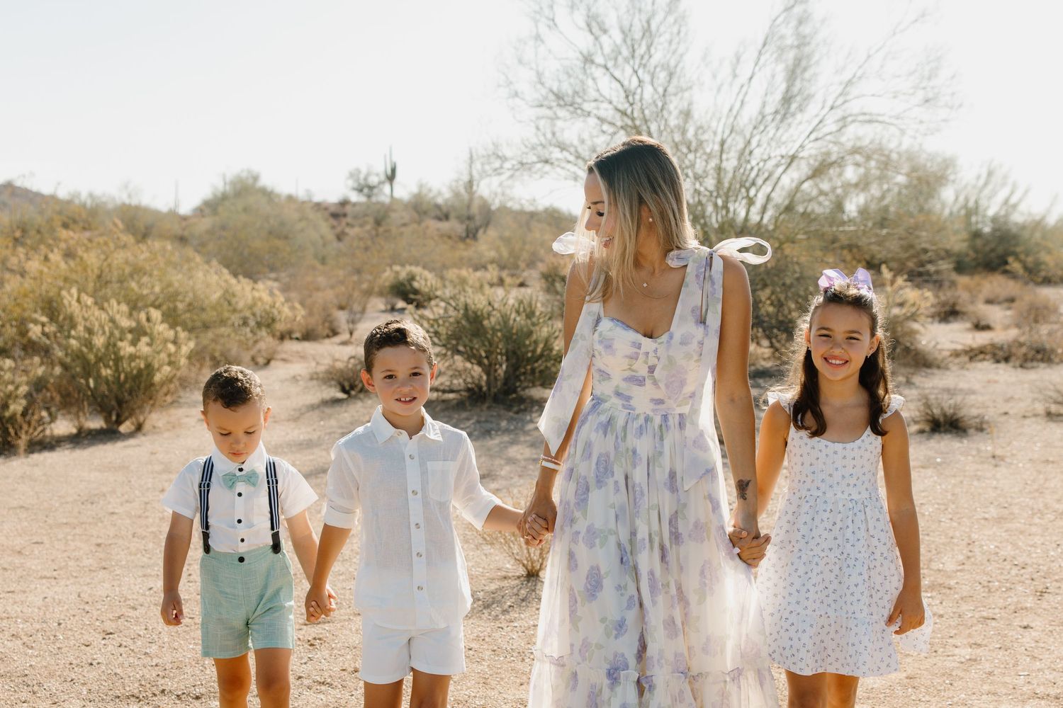 A woman in a floral dress walks with three children in desert landscape, holding hands in coordinated spring outfits.