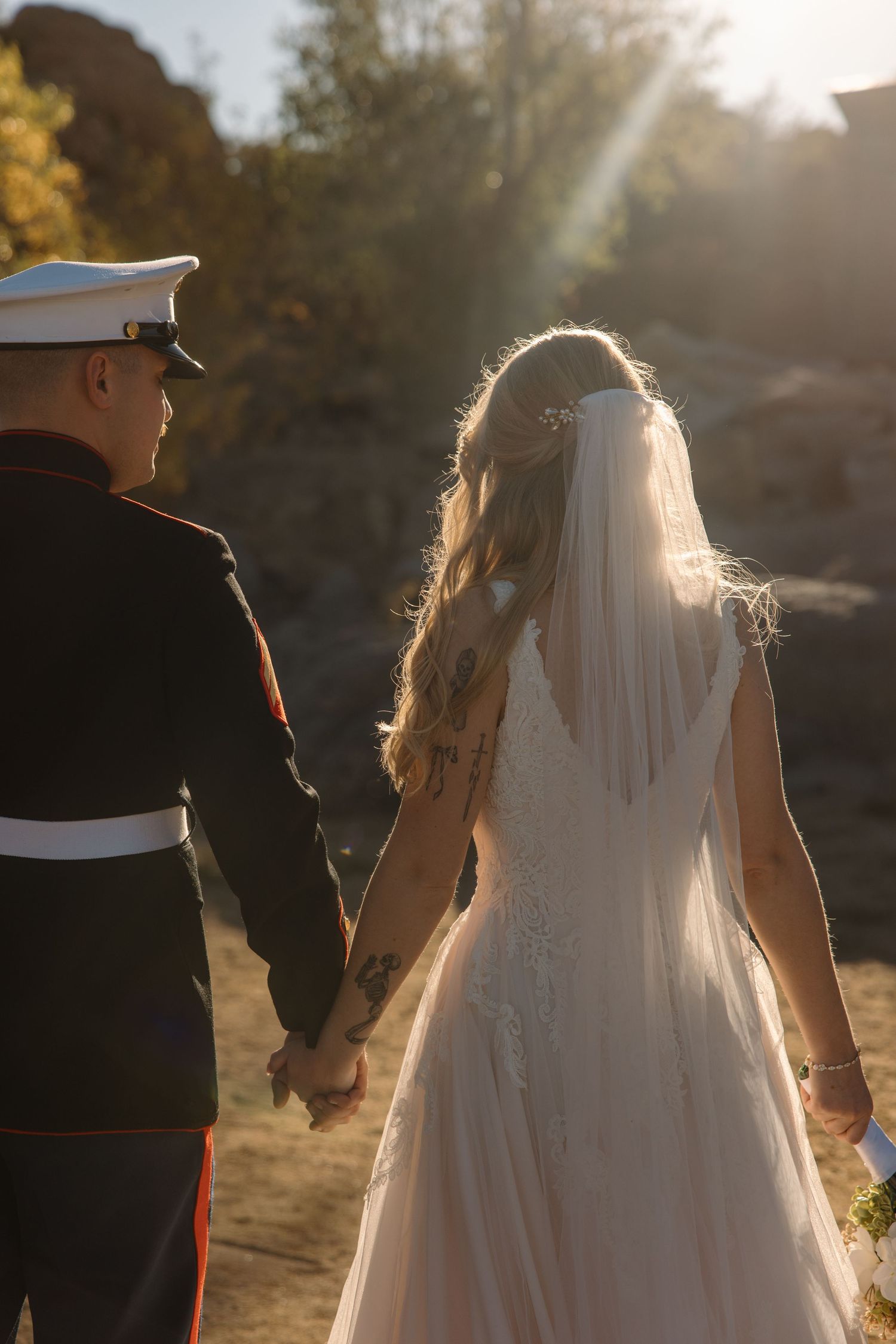 Bride and Marine groom walk hand-in-hand into golden sunset, bride's veil flowing behind her.