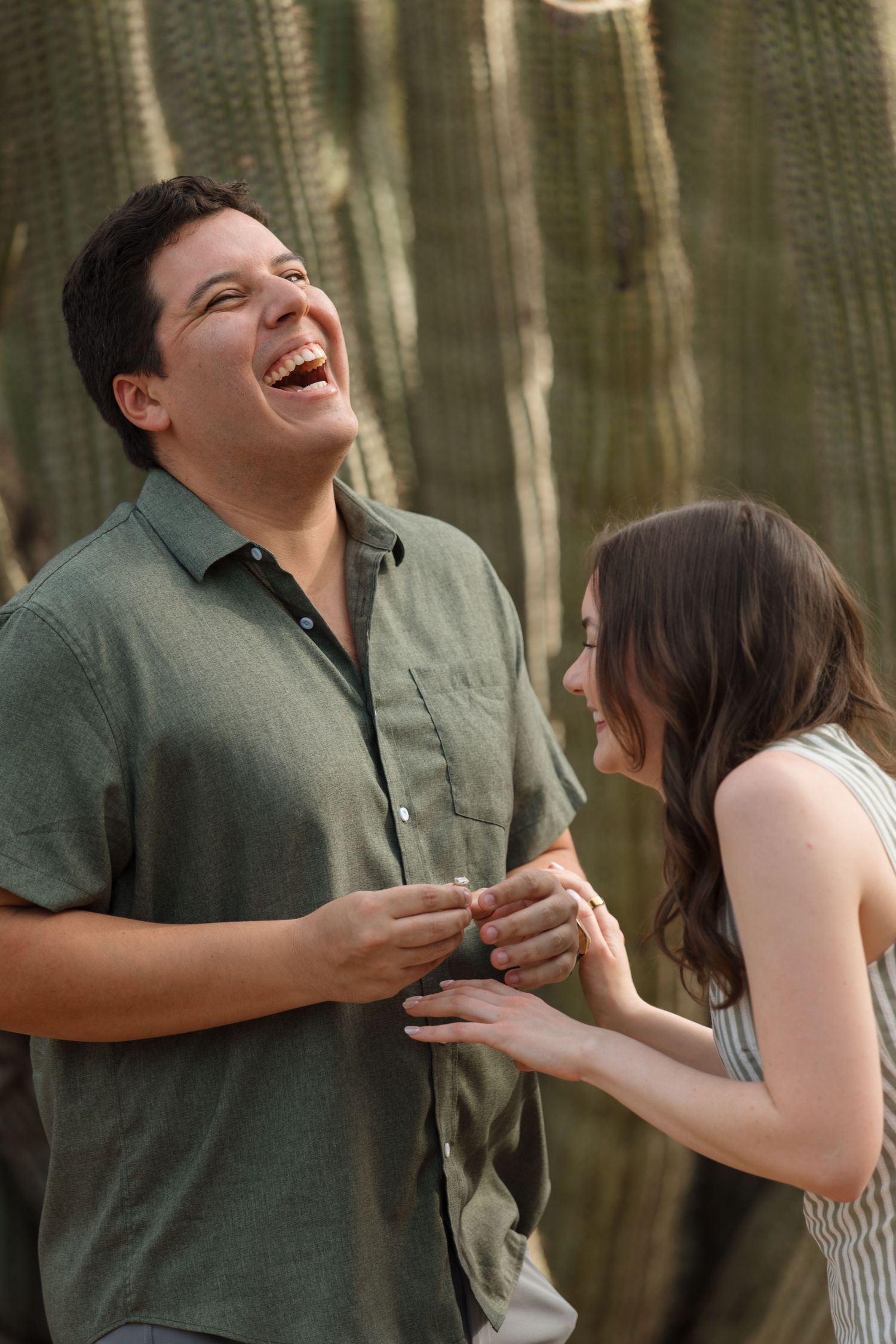 Happy couple laughing together outdoors near a large cactus during an engagement photo session.