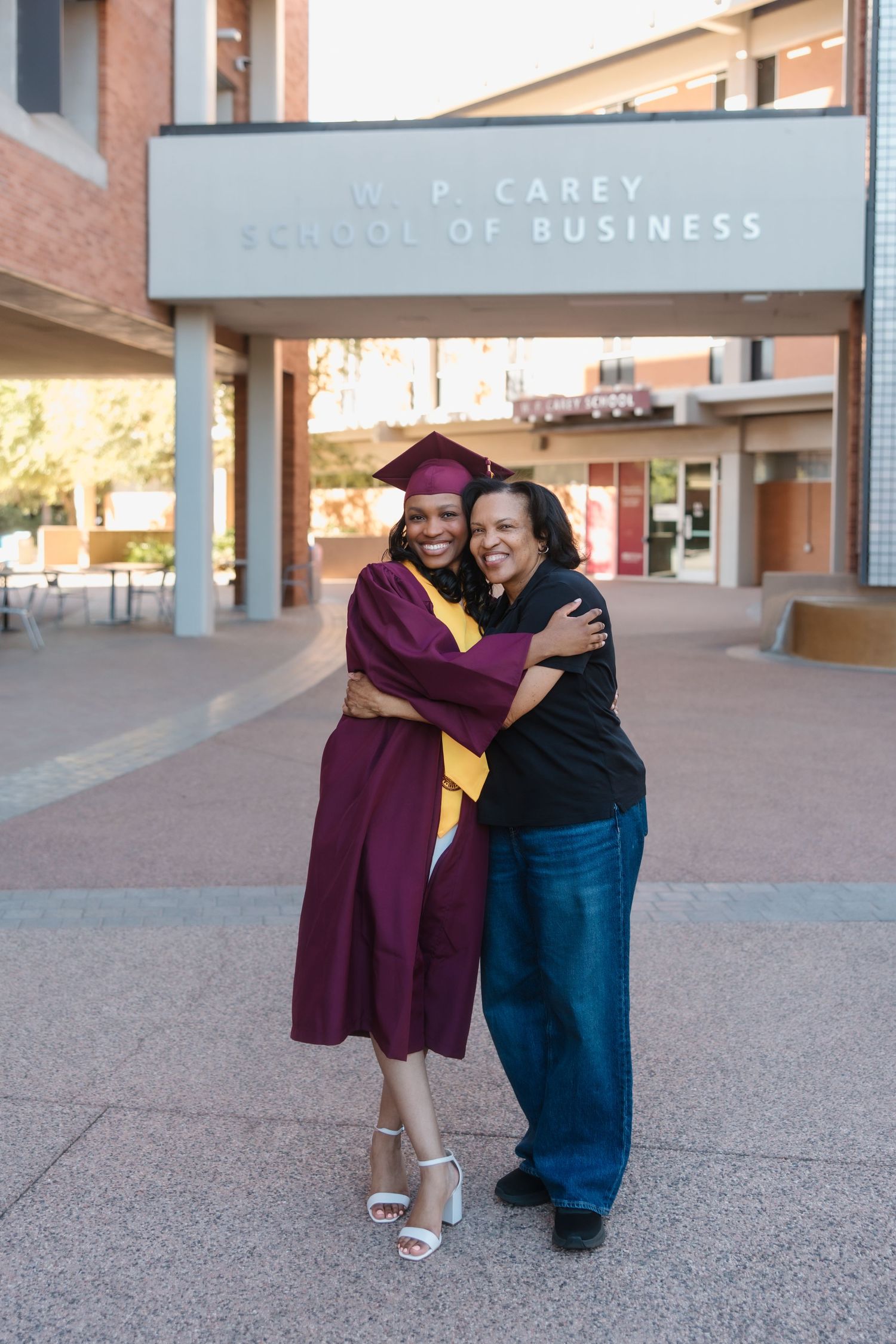 Graduate in maroon cap and gown hugs a woman outside W.P. Carey School of Business building.