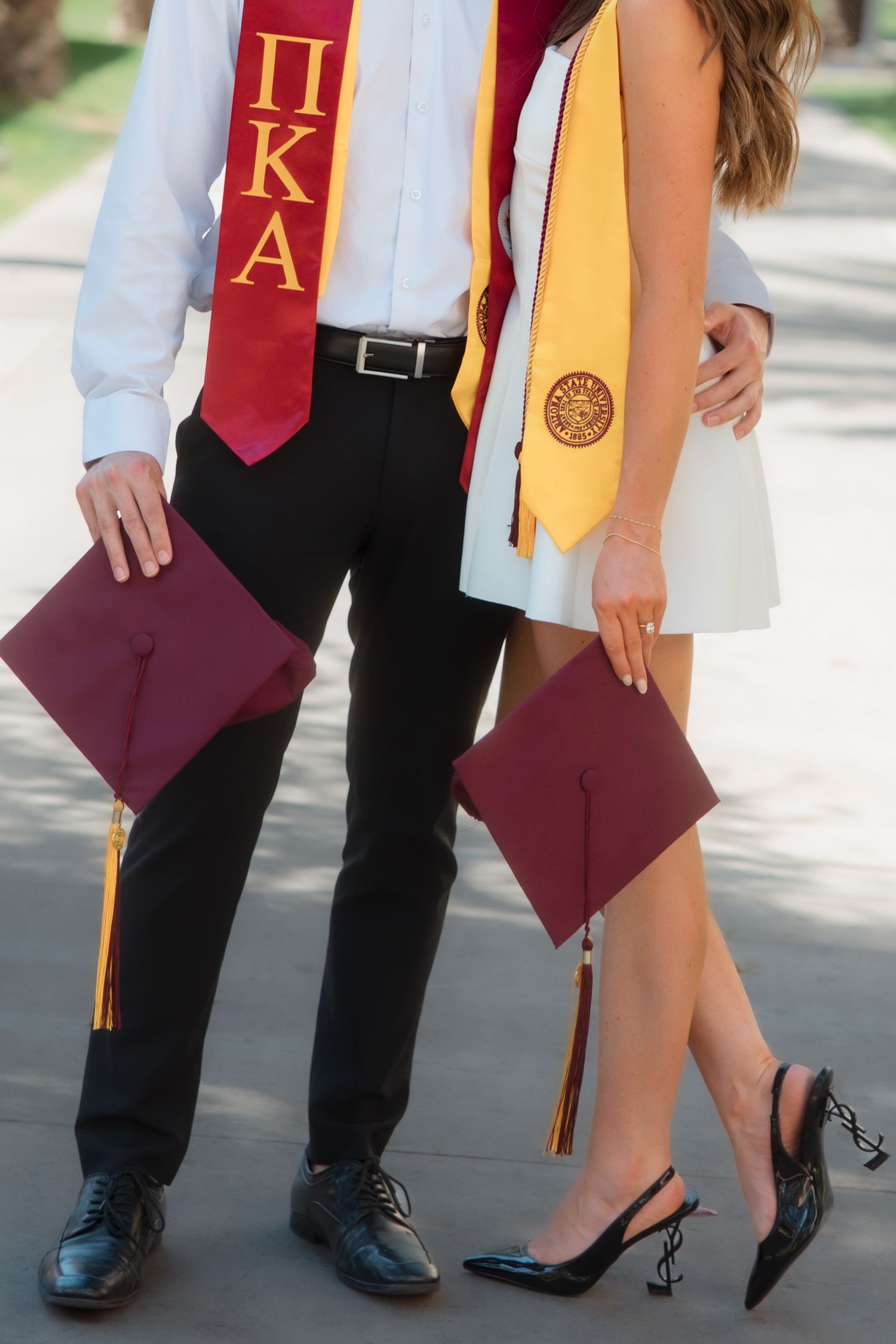 Close-up of graduating couple holding maroon caps, wearing Pi Kappa Alpha and gold stoles.
