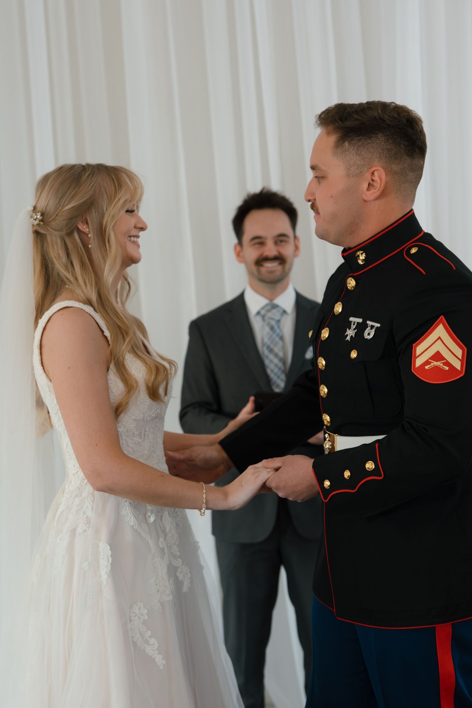 Bride and Marine groom hold hands at altar during wedding ceremony with officiant in background.
