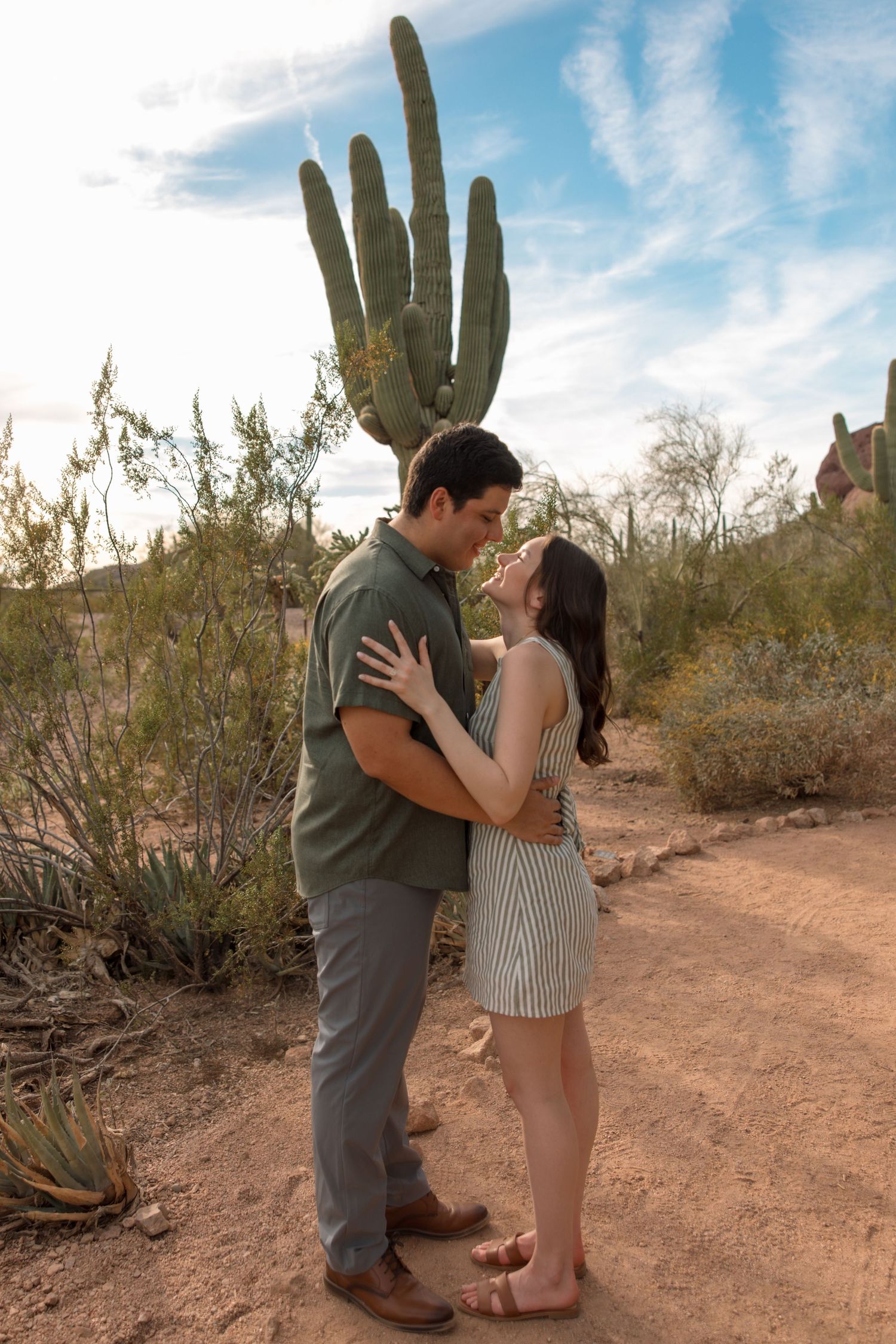 Happy couple sharing romantic kiss while embracing in desert landscape with saguaro cactus.