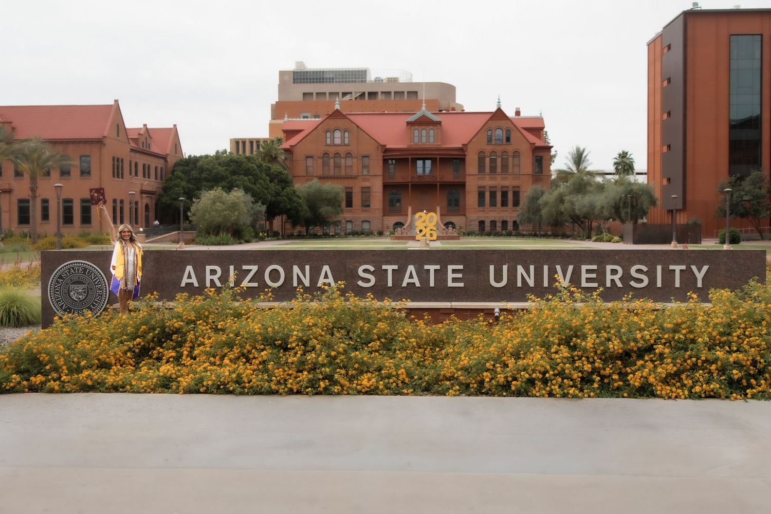Arizona State University sign with red brick buildings and yellow flowers on the Tempe campus.