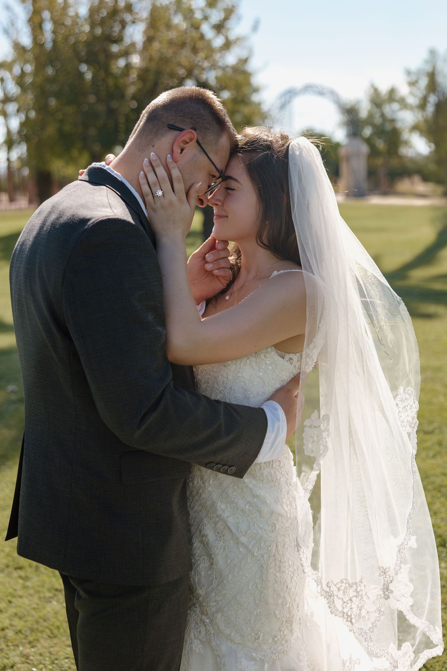 A bride and groom share an intimate moment touching foreheads outdoors on their sunny wedding day.