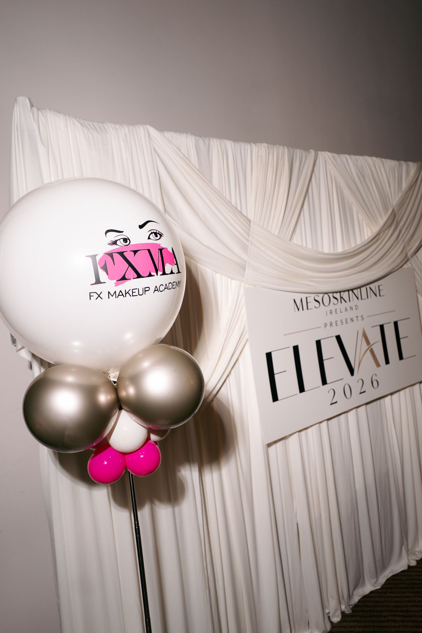 White FX Makeup Academy balloon with silver and pink balloons beside an Elevate 2026 Mesoskinline Ireland sign on a draped white backdrop.